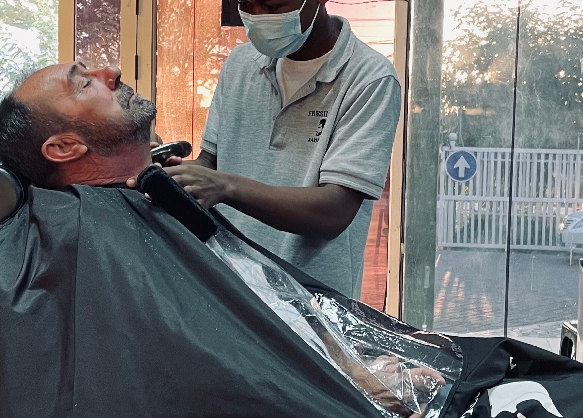 Serviço de barbearia no Fresh Cut Barbershop, Maputo, Maputo, MZ. Cliente relaxa enquanto barbeiro trabalha.