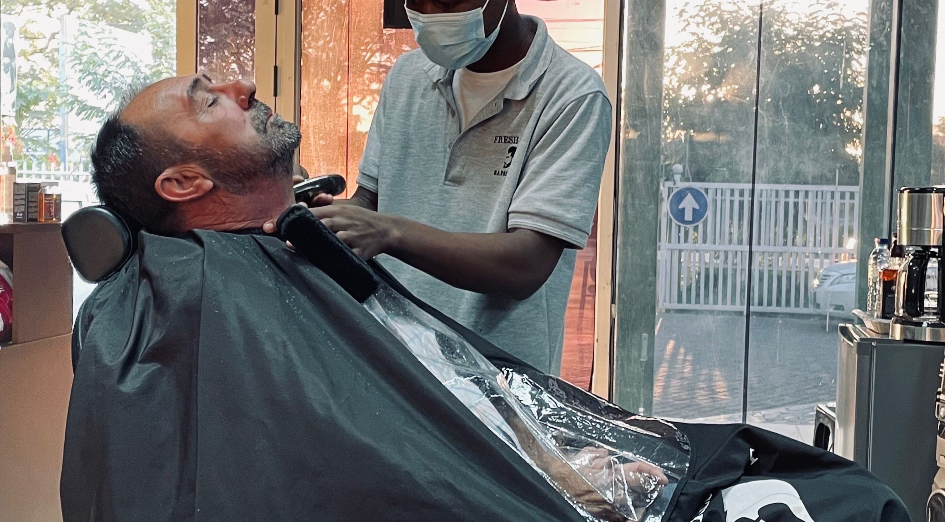 Serviço de barbearia no Fresh Cut Barbershop, Maputo, Maputo, MZ. Cliente relaxa enquanto barbeiro trabalha.