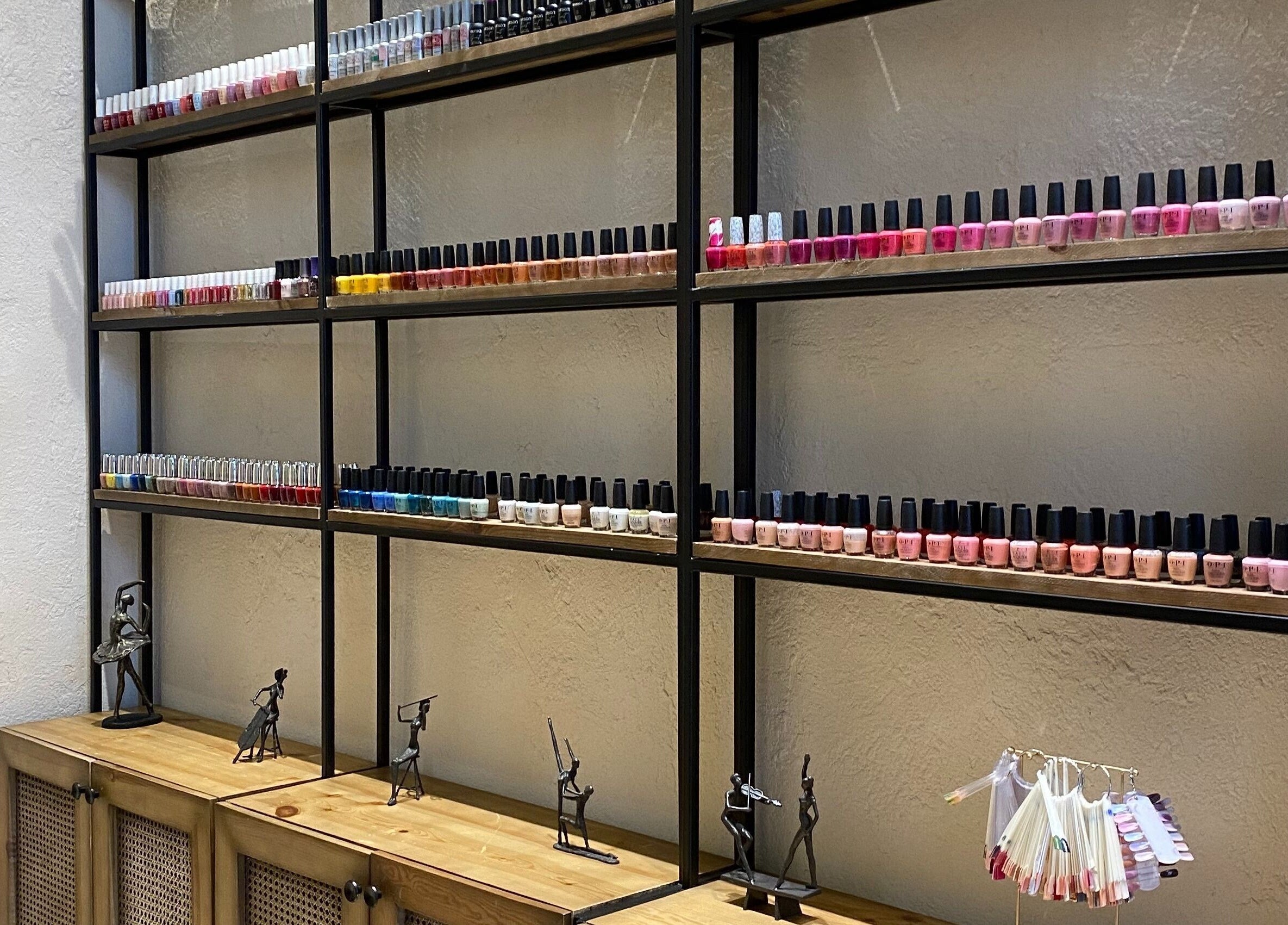 Nail polish collection at The Bliss Nails, Riyadh, SA, showcasing diverse colors on stylish shelves.