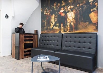 Rembrandt Barbershop in Leiden, Zuid-holland, NL, met chique zwarte wachtbank en kunstwerk op de muur.