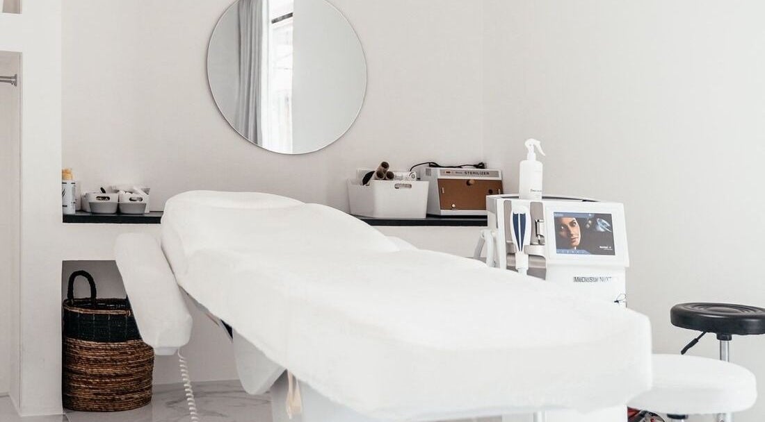 Modern treatment room at LASER ME ULUWATU in Bali, Bali, ID with a sleek massage bed and round mirror.