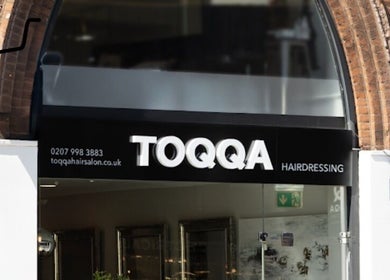 Entrance of TOQQA Hair Salon in London, England, GB with modern signage and brick archway.