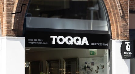 Entrance of TOQQA Hair Salon in London, England, GB with modern signage and brick archway.