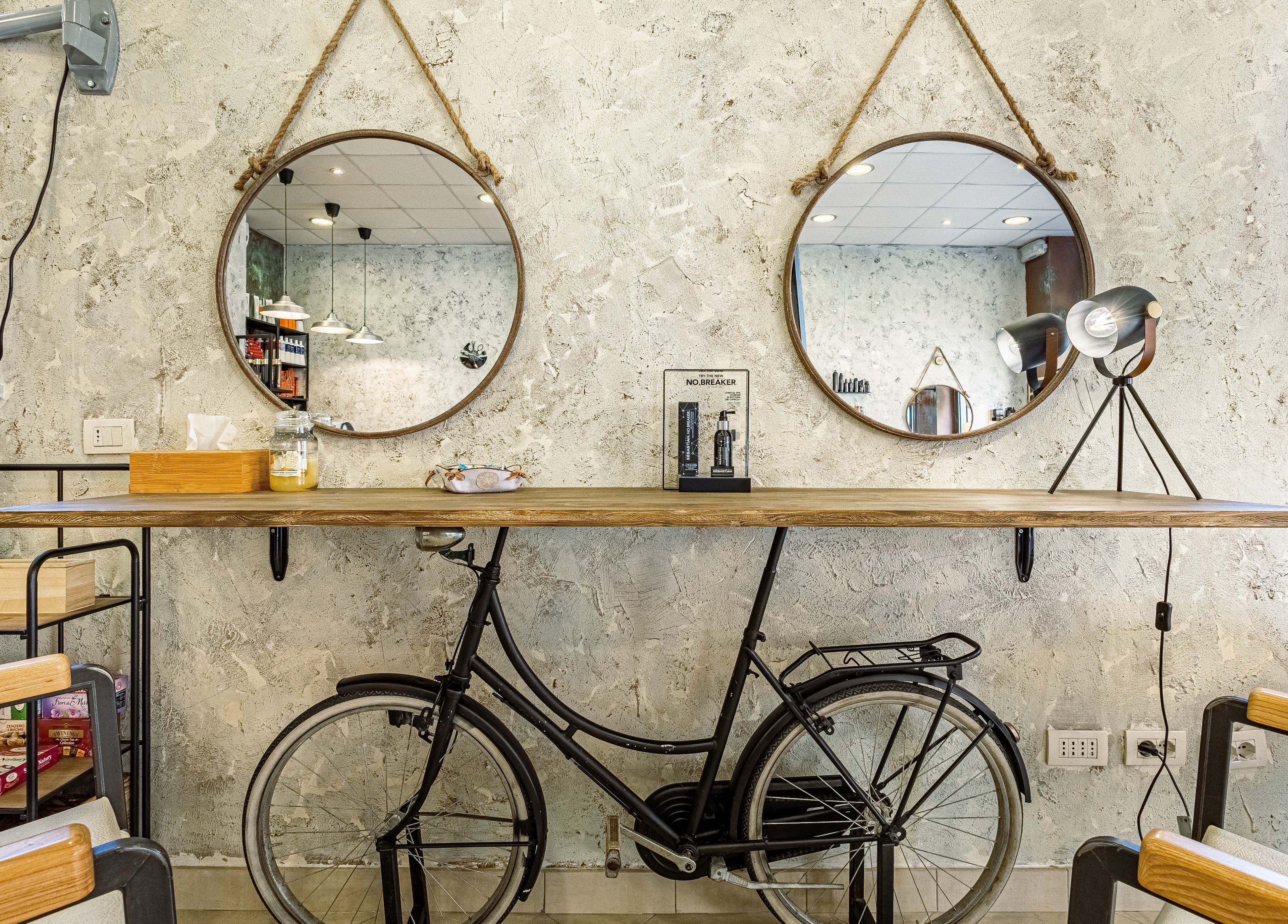 Interno di L’officina Del Capello a Sanremo con specchi rotondi e bici decorativa.