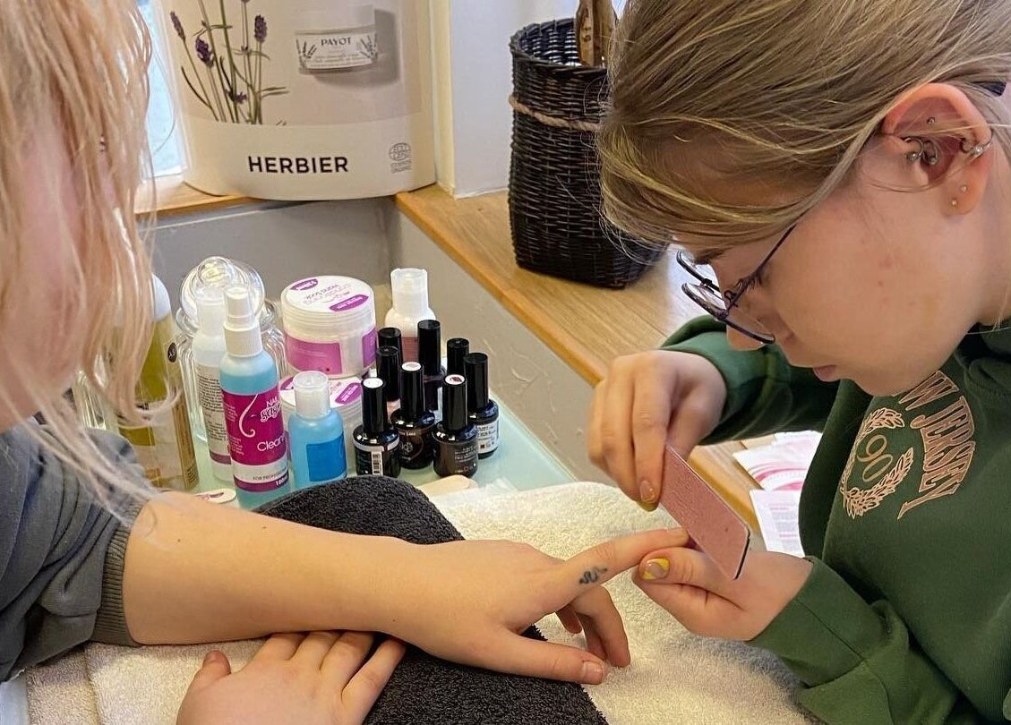 Student performing nail care at Bay Beauty Academy, Whitley Bay, England, GB. Nail polish bottles visible.