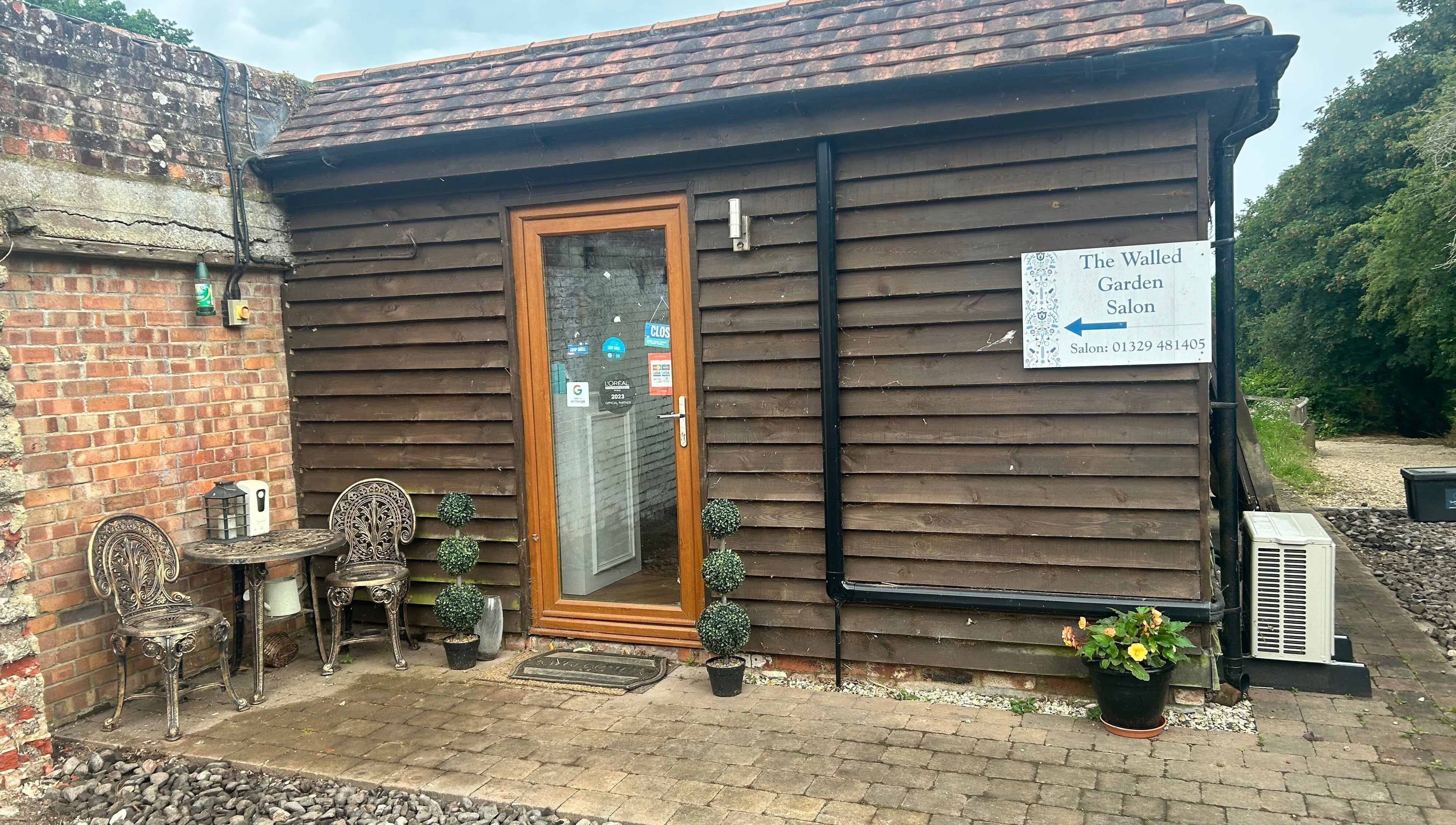 Entrance of The Walled Garden Salon, Fareham, England, GB, featuring a rustic door and outdoor seating.