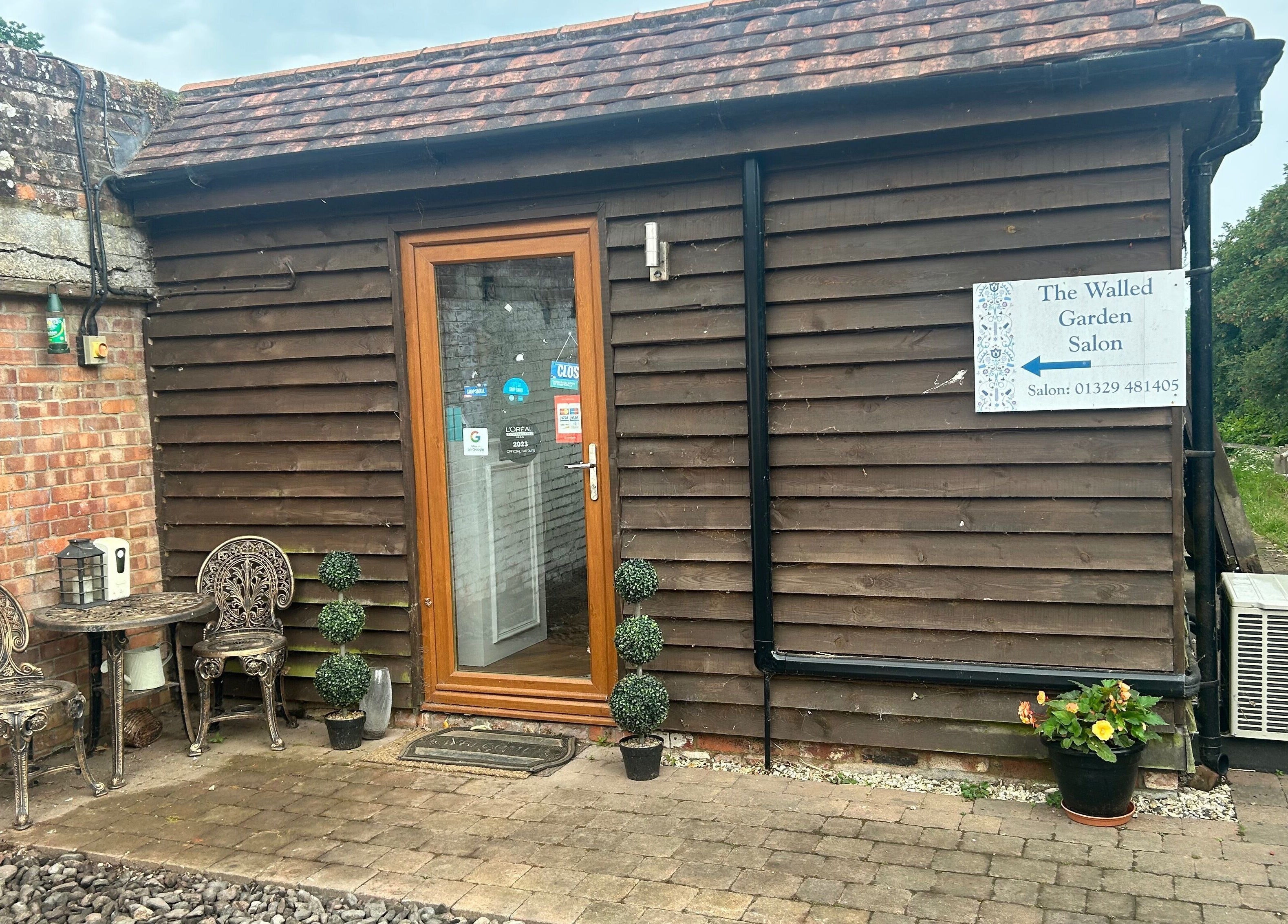 Entrance of The Walled Garden Salon, Fareham, England, GB, featuring a rustic door and outdoor seating.