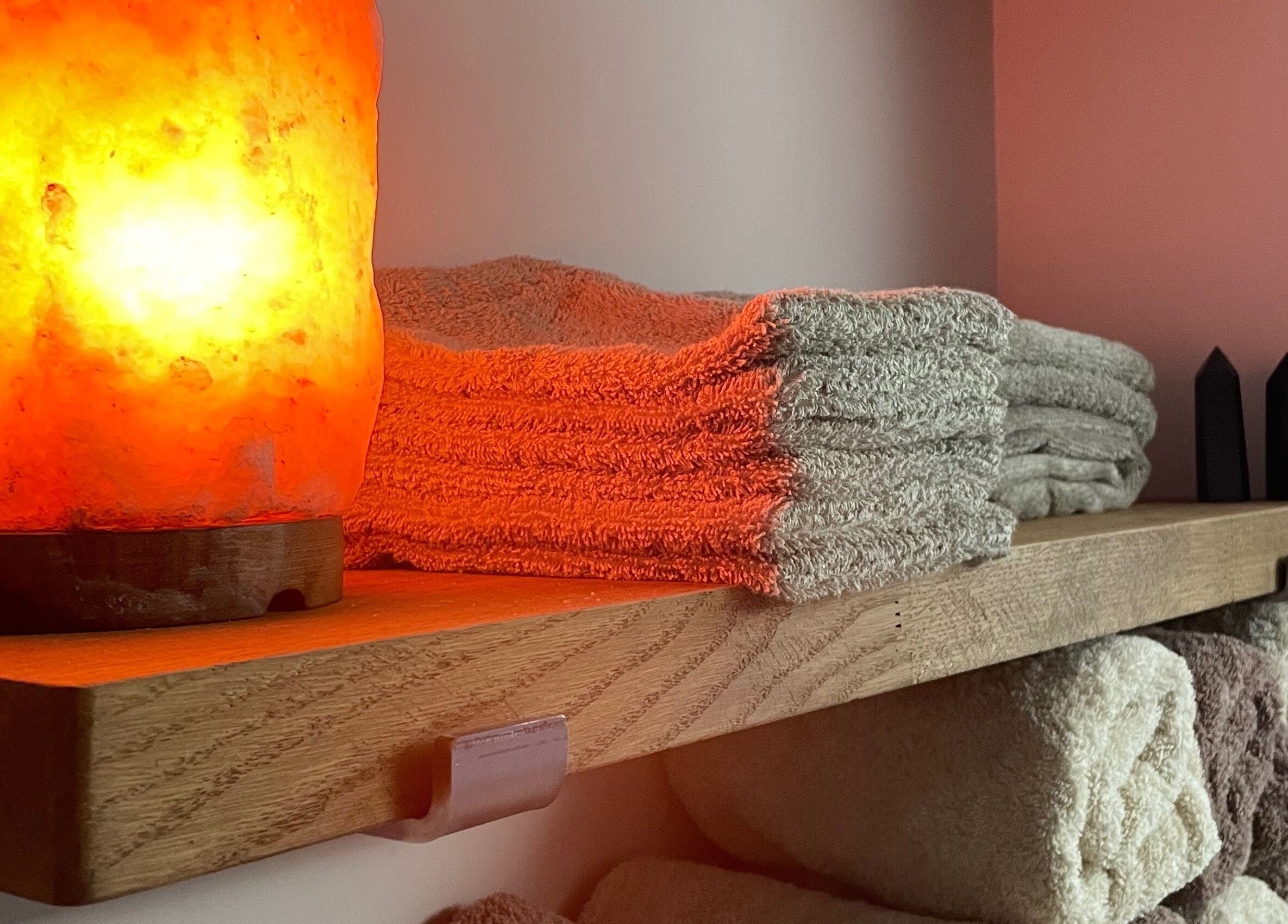 Warm-lit salt lamp and neatly stacked towels at Living Well Reflexology, Mickleton, England, GB.