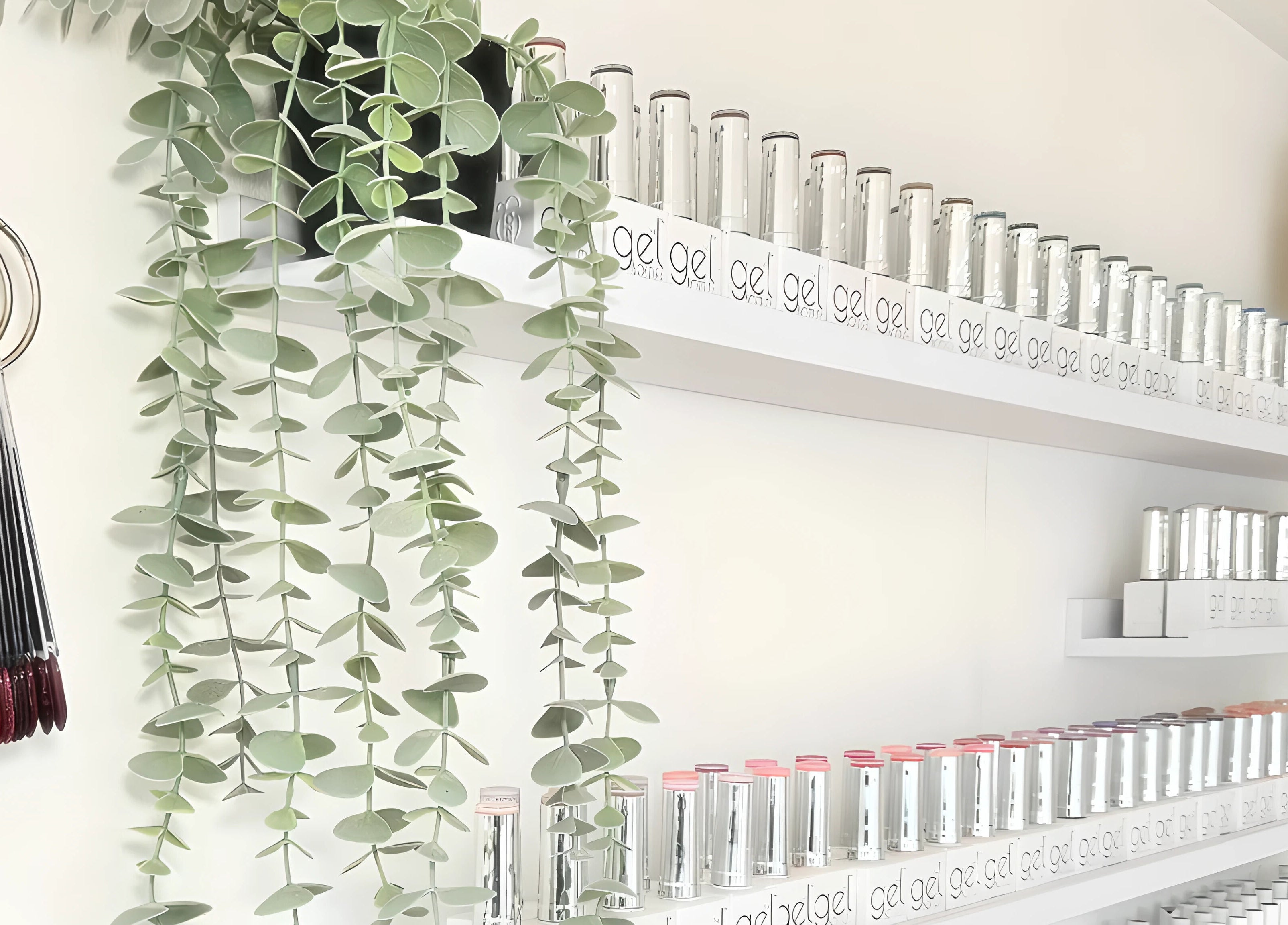 Nail polish collection on white shelves at Babe Cave, Birkenhead, England, GB, with elegant greenery decor.