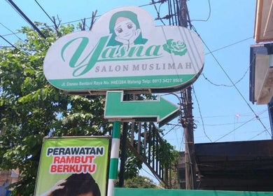Entrance sign of Salon Muslimah YASNA, Malang, Jawa Timur, ID, nestled among green trees.