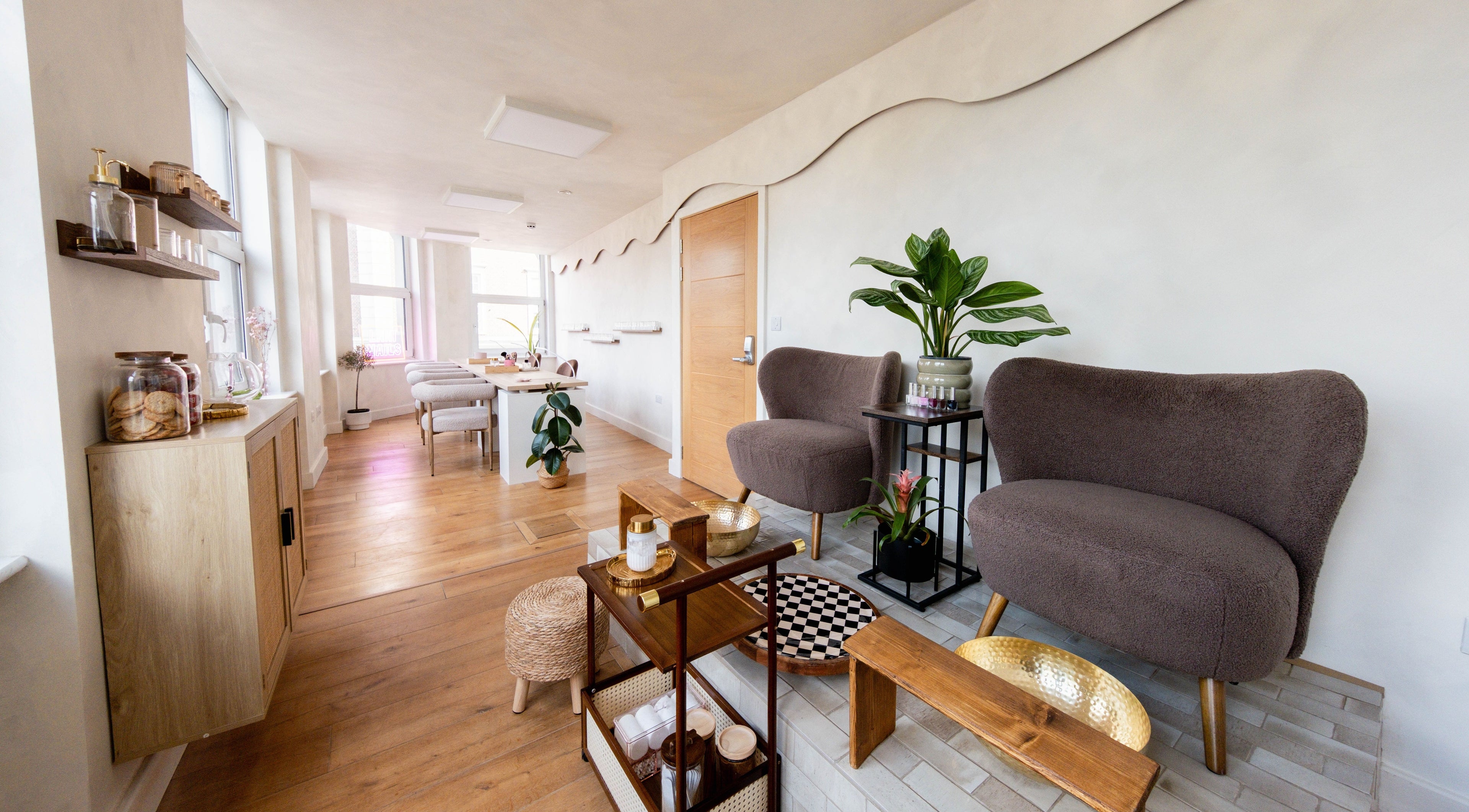 Cozy seating area at Lani Nails London, GB with plush chairs, indoor plants, and wooden decor.