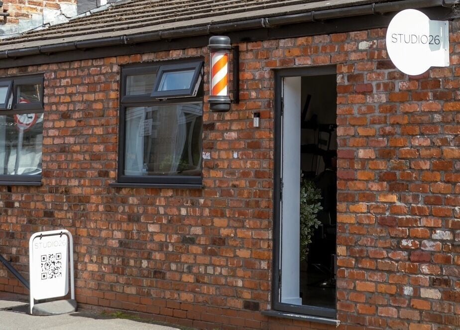 Exterior of STUDIO26 Barbershop in Hazel Grove, England, GB showing brick building and barber pole.