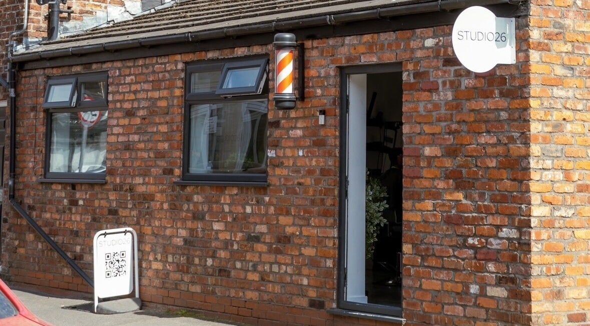 Exterior of STUDIO26 Barbershop in Hazel Grove, England, GB showing brick building and barber pole.