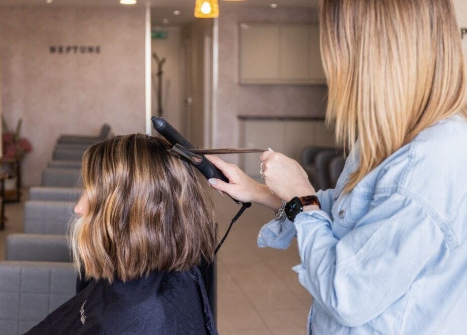 Hairstylist using a flat iron on a client at Neptune salon in Livingston, Scotland, GB.