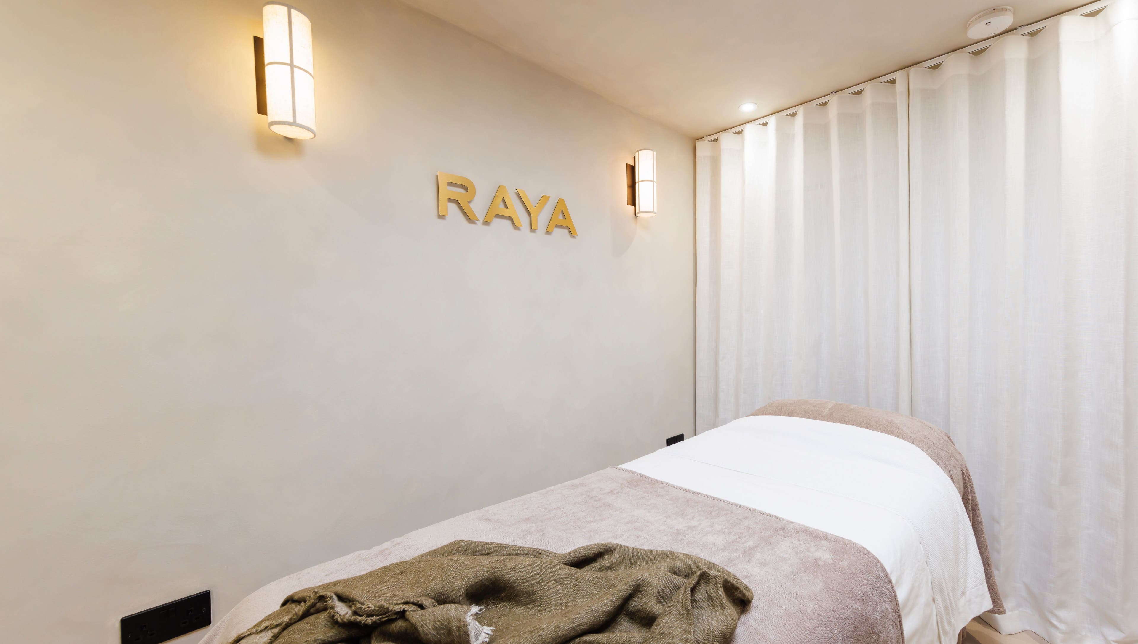 Relaxing treatment room at Raya Clinic - Skin, PMU & Aesthetics, Havant, England, GB, with a cozy bed and soft lighting.