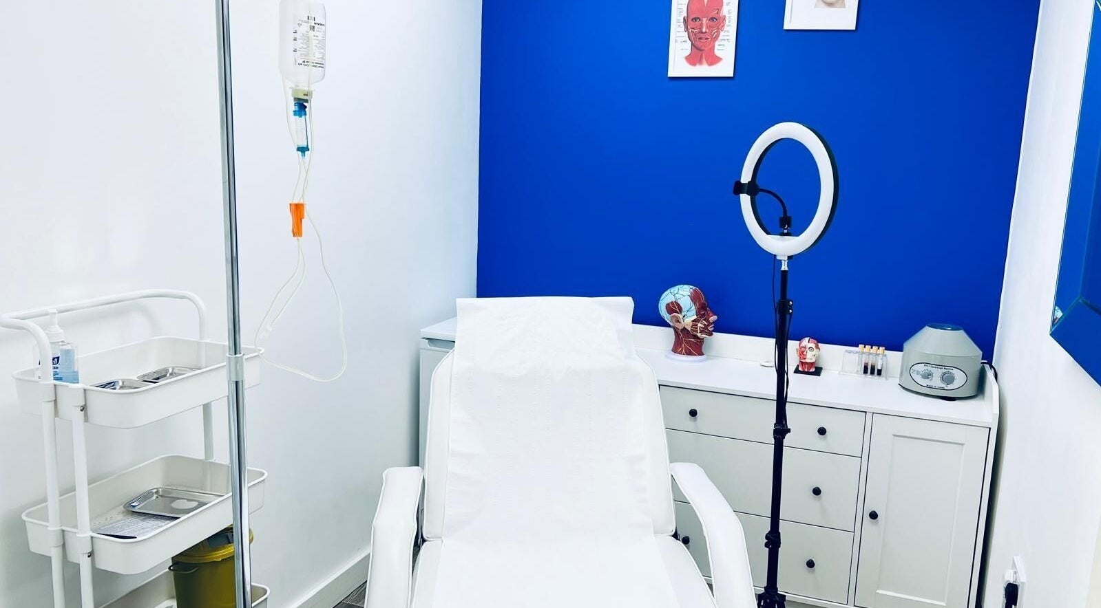Modern treatment room at Beautifly Romford, England with white chair and vibrant blue wall.