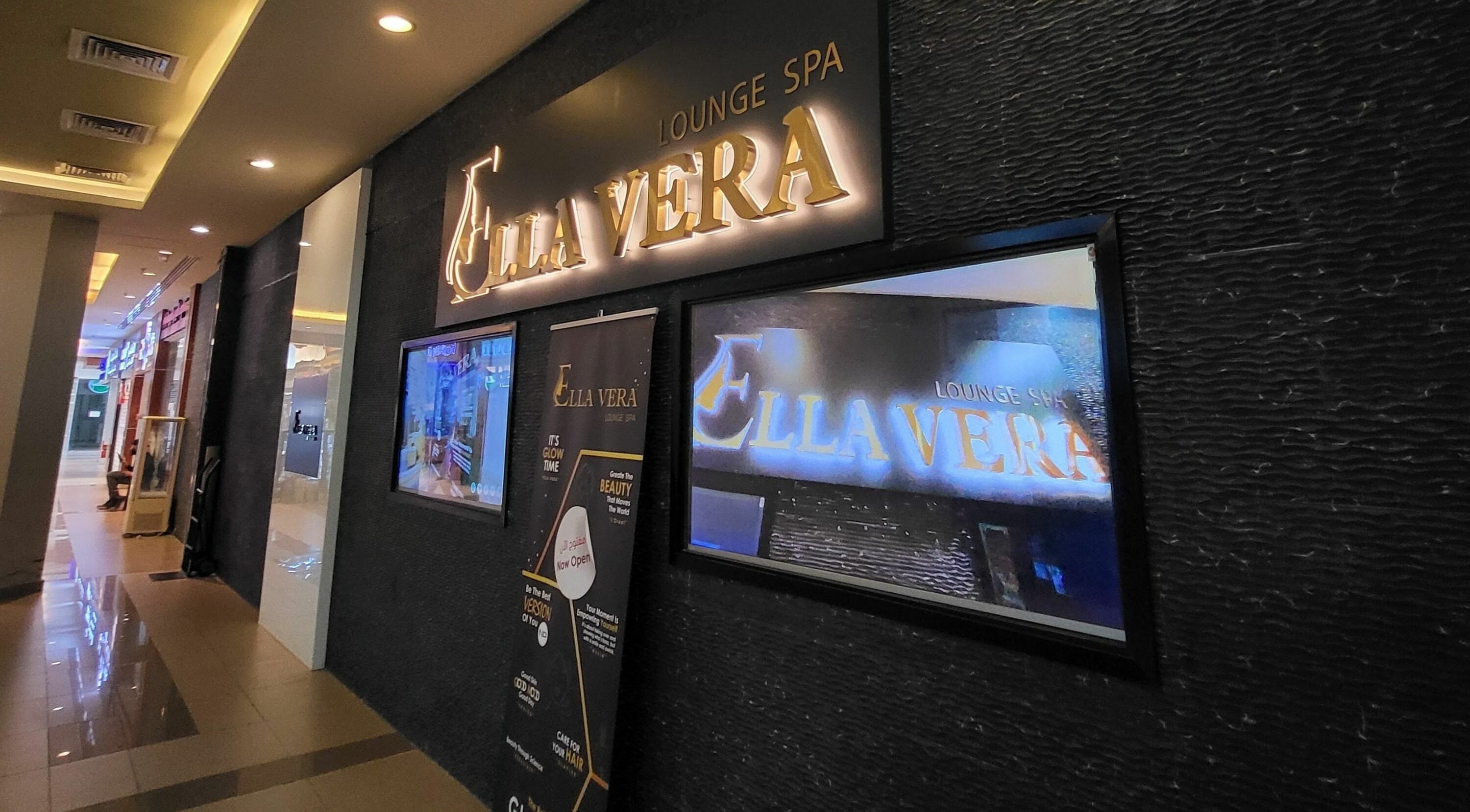 Entrance of Ella Vera Lounge Spa in Al Ain, AE, featuring illuminated signage and stylish interior design.