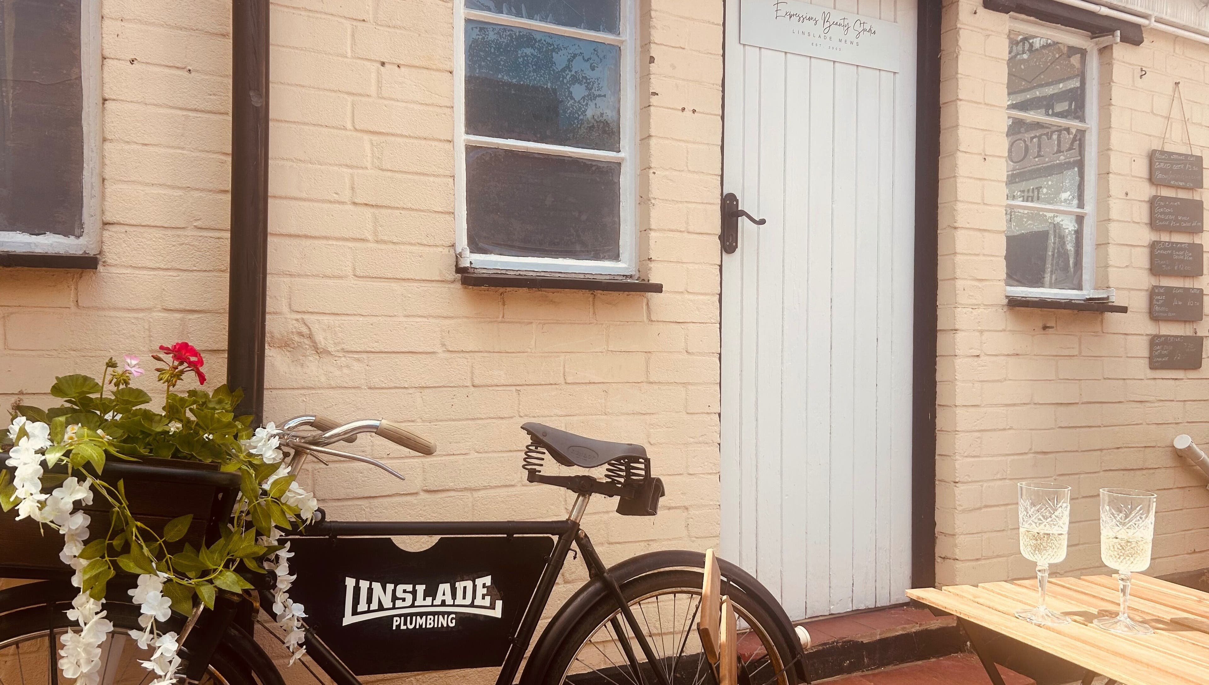 Vintage bike and white door of Expressions Beauty Studios in Leighton Buzzard, England, GB with blooming flowers.