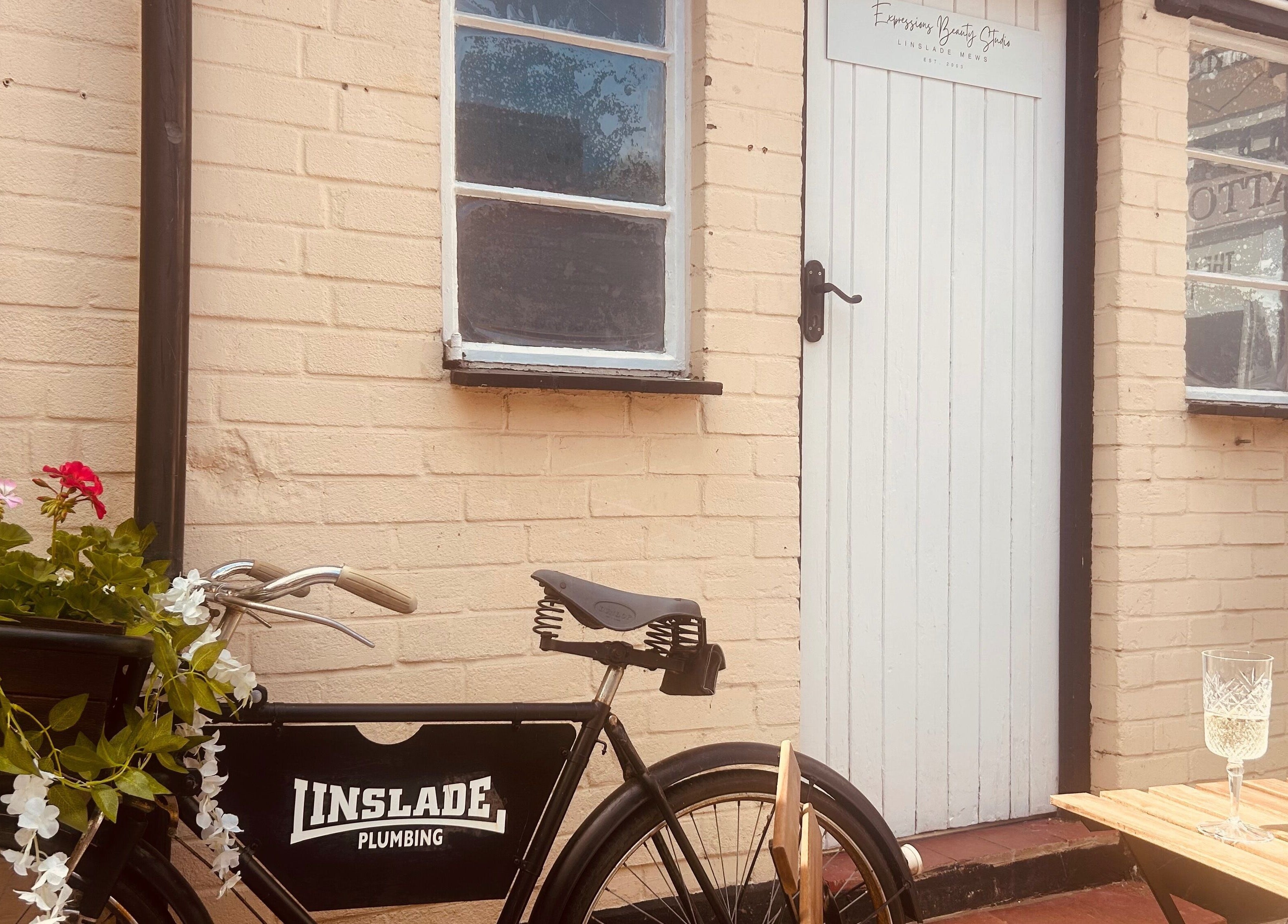 Vintage bike and white door of Expressions Beauty Studios in Leighton Buzzard, England, GB with blooming flowers.