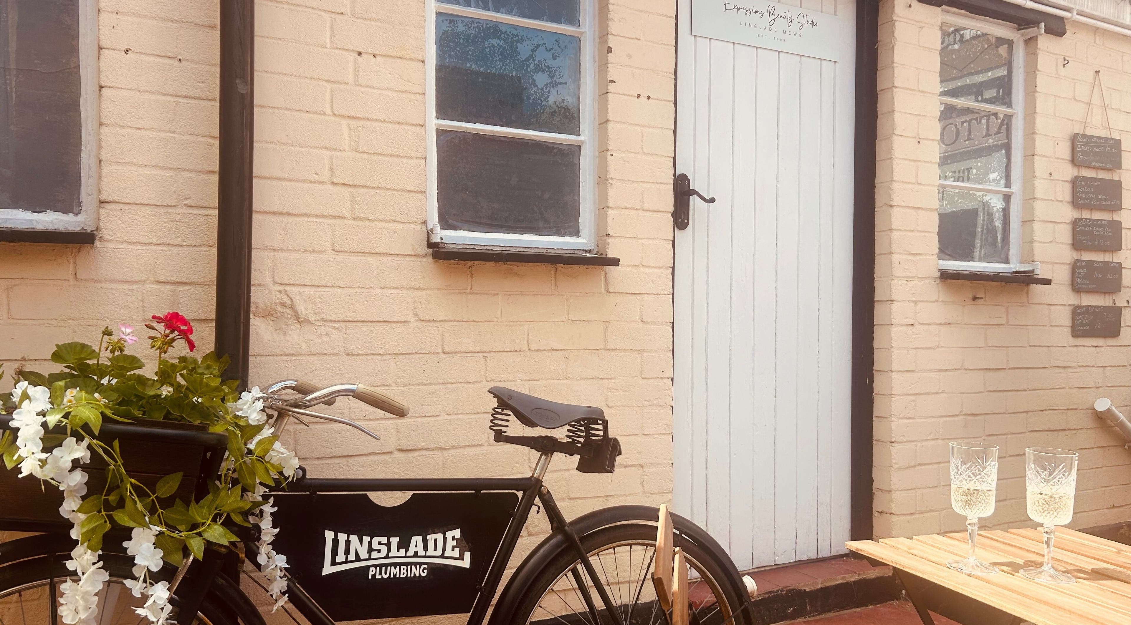 Vintage bike and white door of Expressions Beauty Studios in Leighton Buzzard, England, GB with blooming flowers.