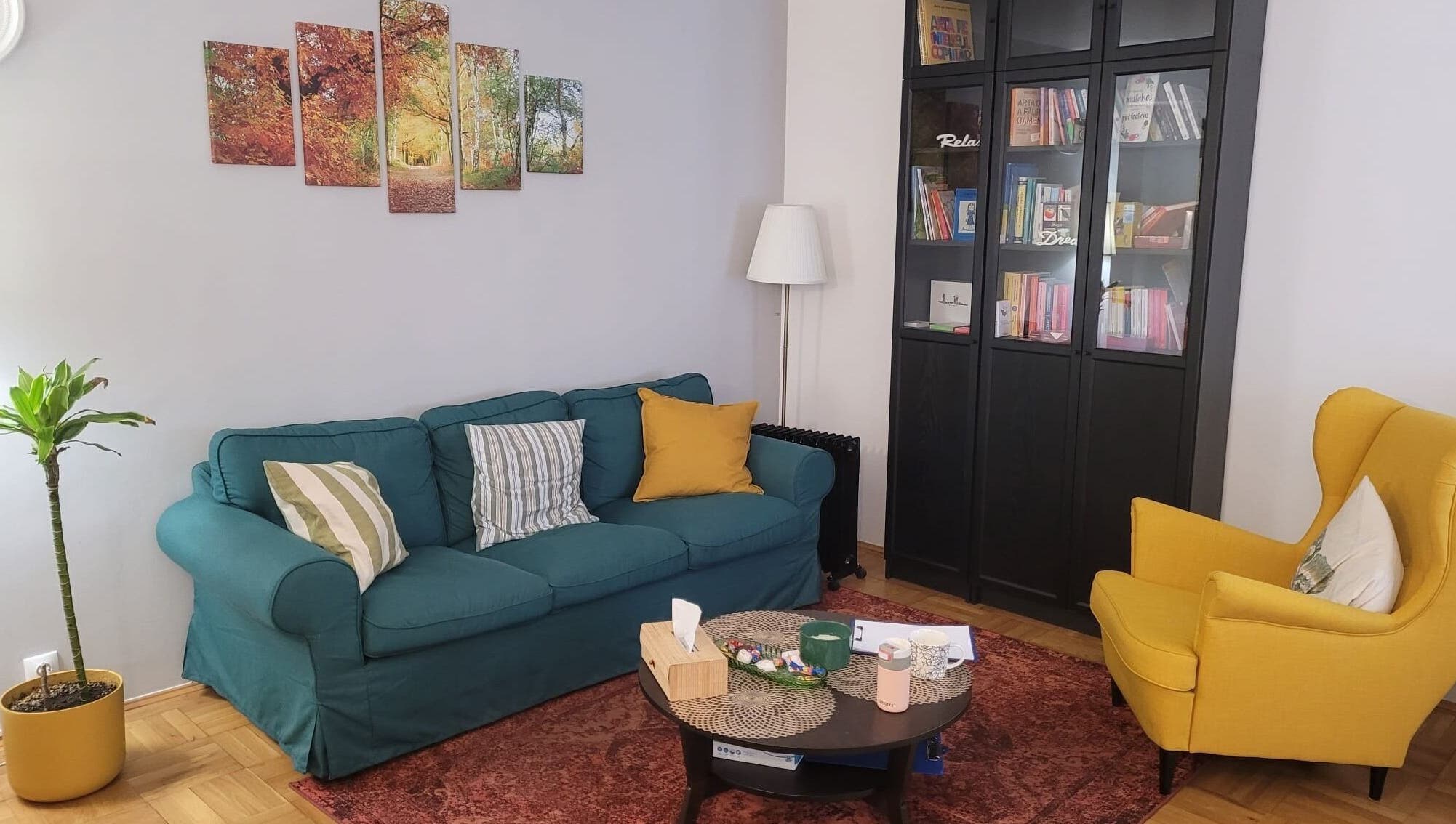 Interior la Cabinet De Psihologie Dumbraveanu Jeni Georgiana, București, cu canapea, fotoliu galben și bibliotecă.