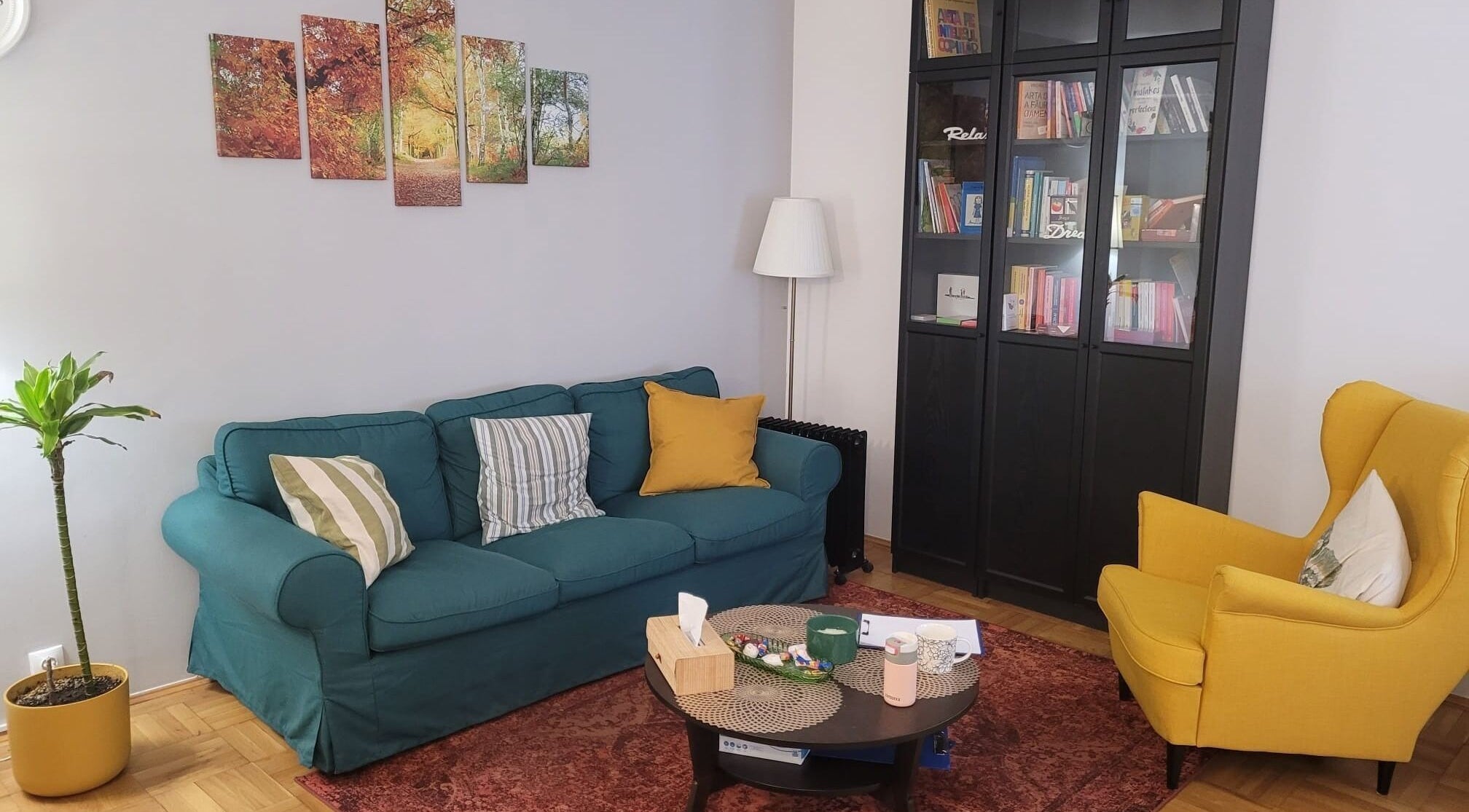 Interior la Cabinet De Psihologie Dumbraveanu Jeni Georgiana, București, cu canapea, fotoliu galben și bibliotecă.
