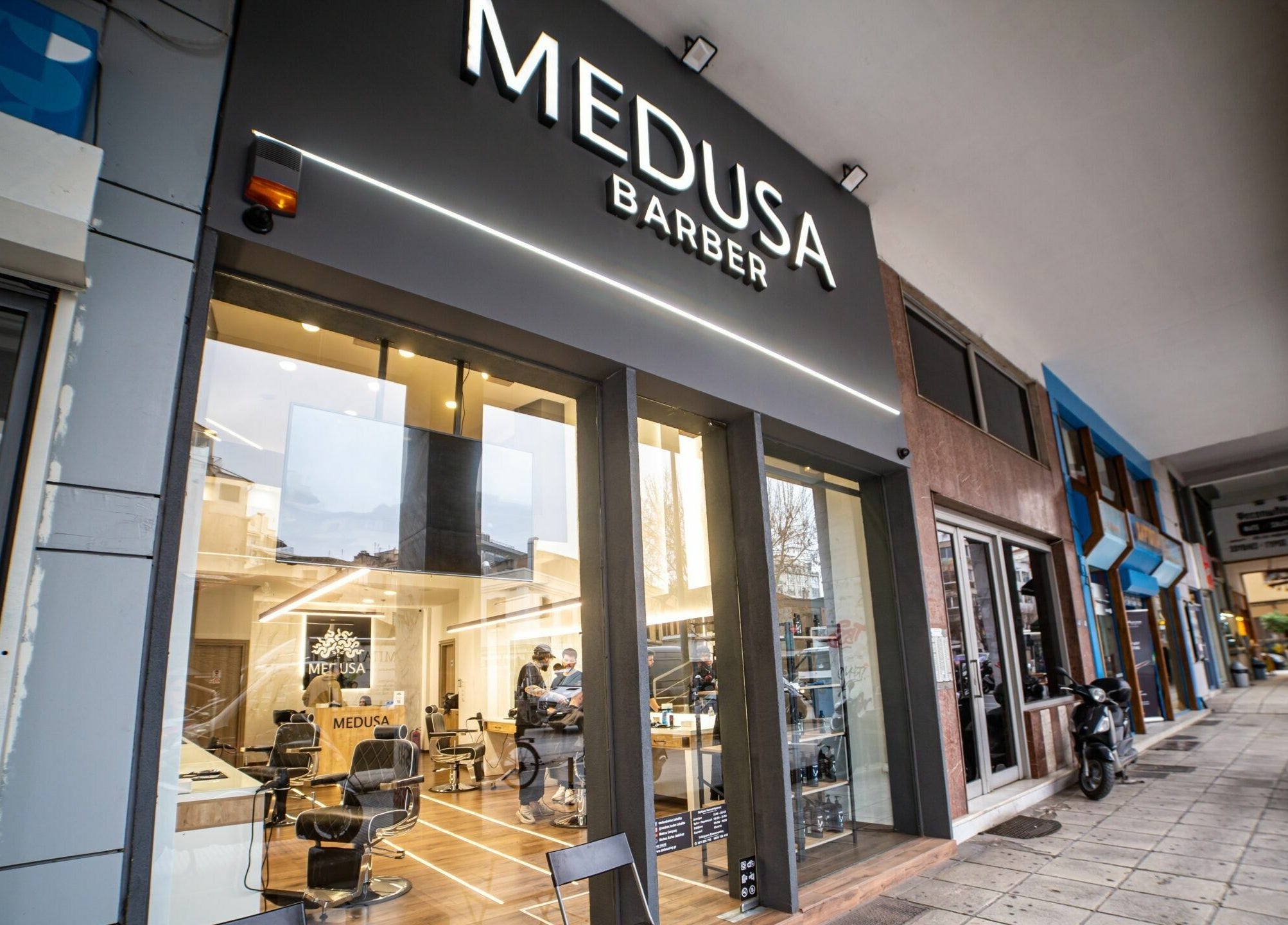 Είσοδος του Medusa Barber στη Θεσσαλονίκη, GR με μοντέρνα επιγραφή και γυάλινη πρόσοψη.