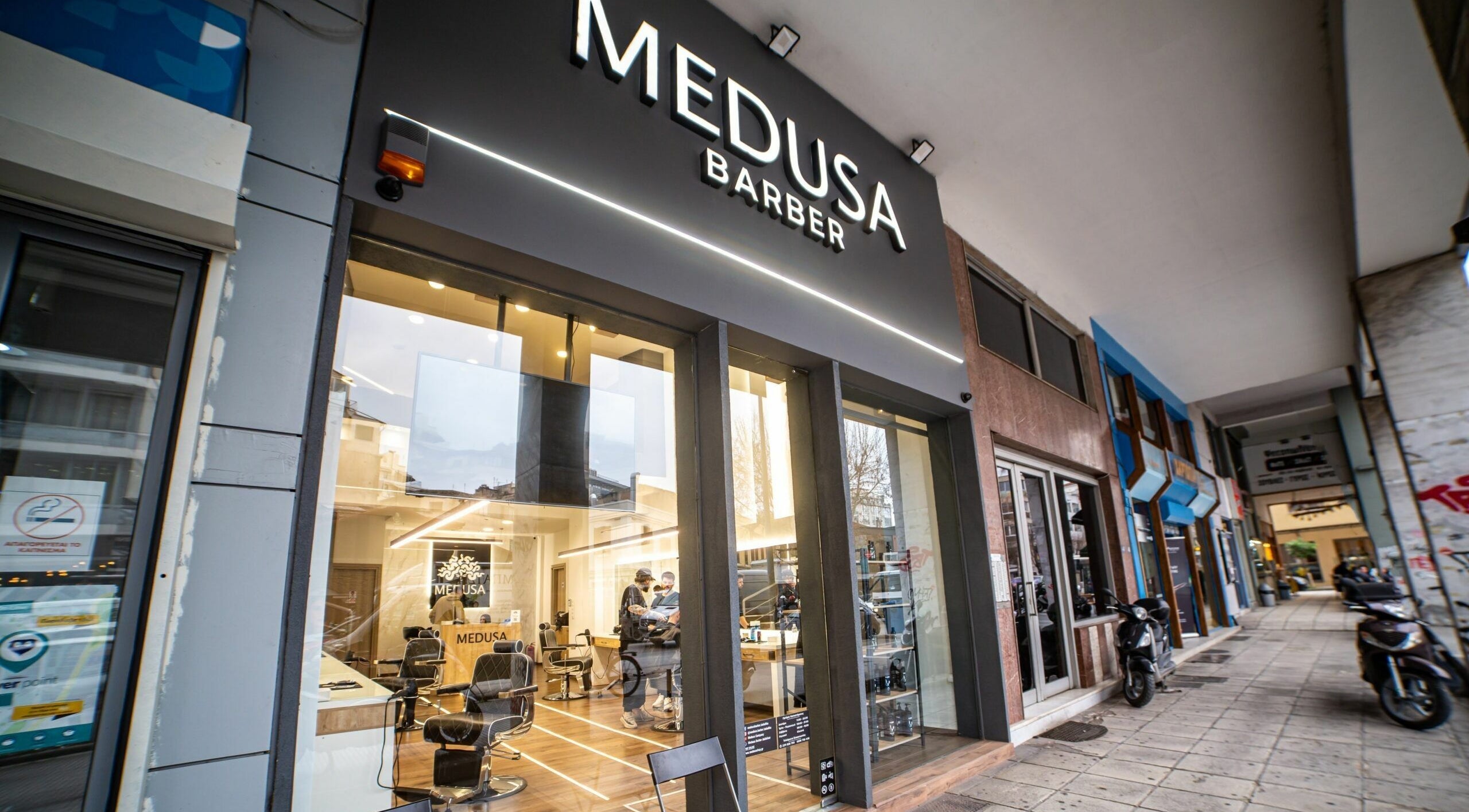 Είσοδος του Medusa Barber στη Θεσσαλονίκη, GR με μοντέρνα επιγραφή και γυάλινη πρόσοψη.