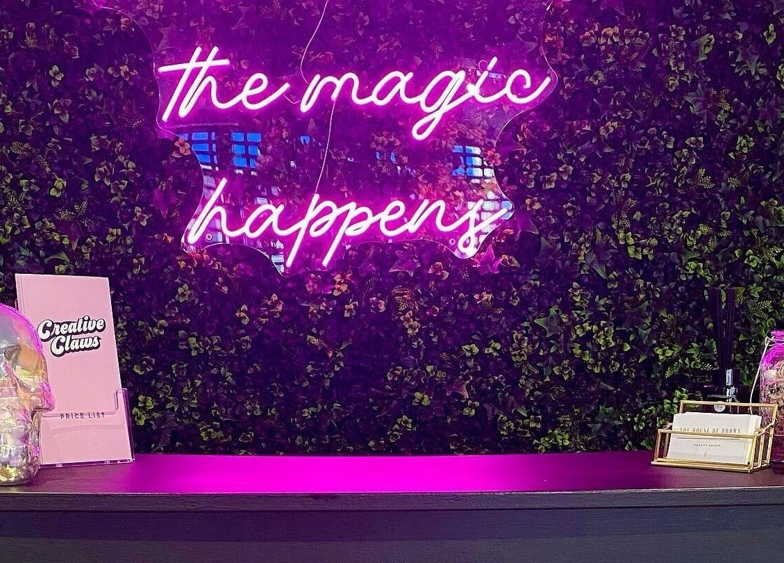 Vibrant neon sign on lush backdrop at Creative Claws Salon and Training Academy, Holyhead, Wales, GB.