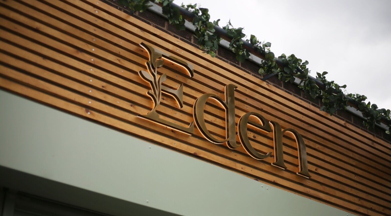 Elegant wooden sign of Eden Salon in Tyldesley, England, GB with lush greenery on top.