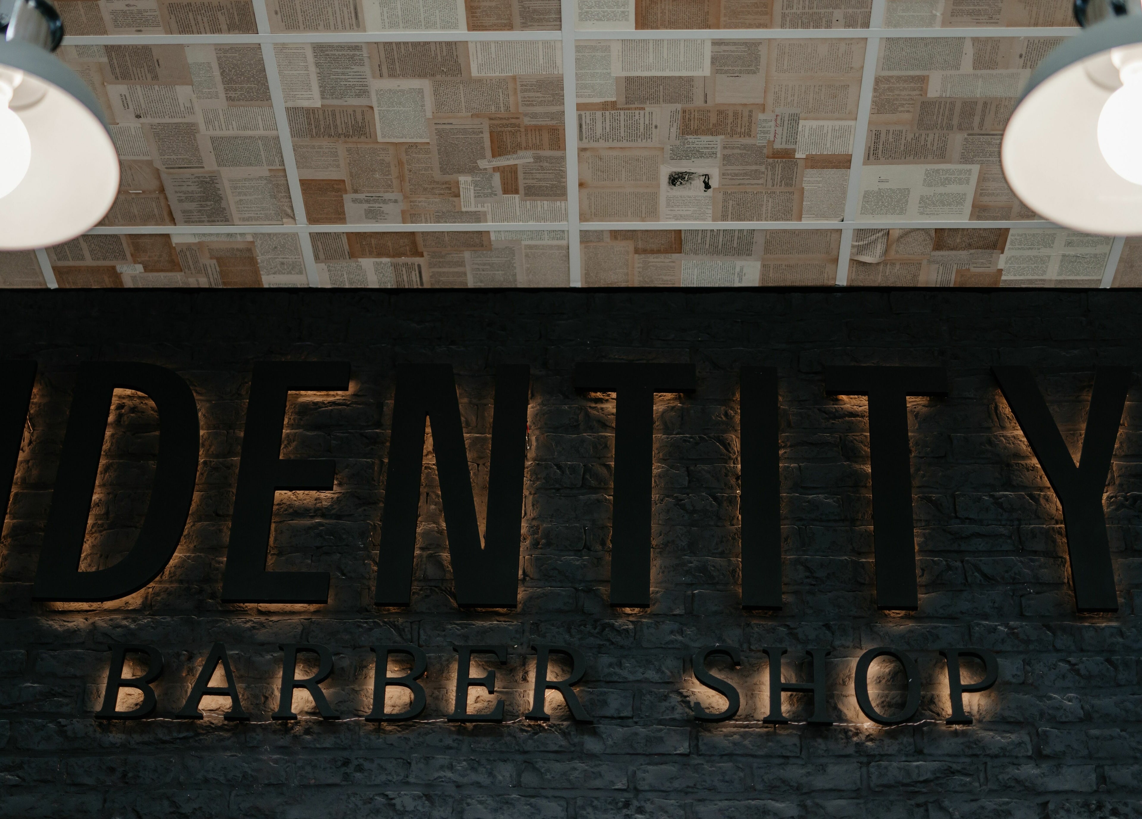 Logo iluminat la Identity Barber Shop, Cluj-Napoca, România, RO, cu tavan decorativ de ziare.