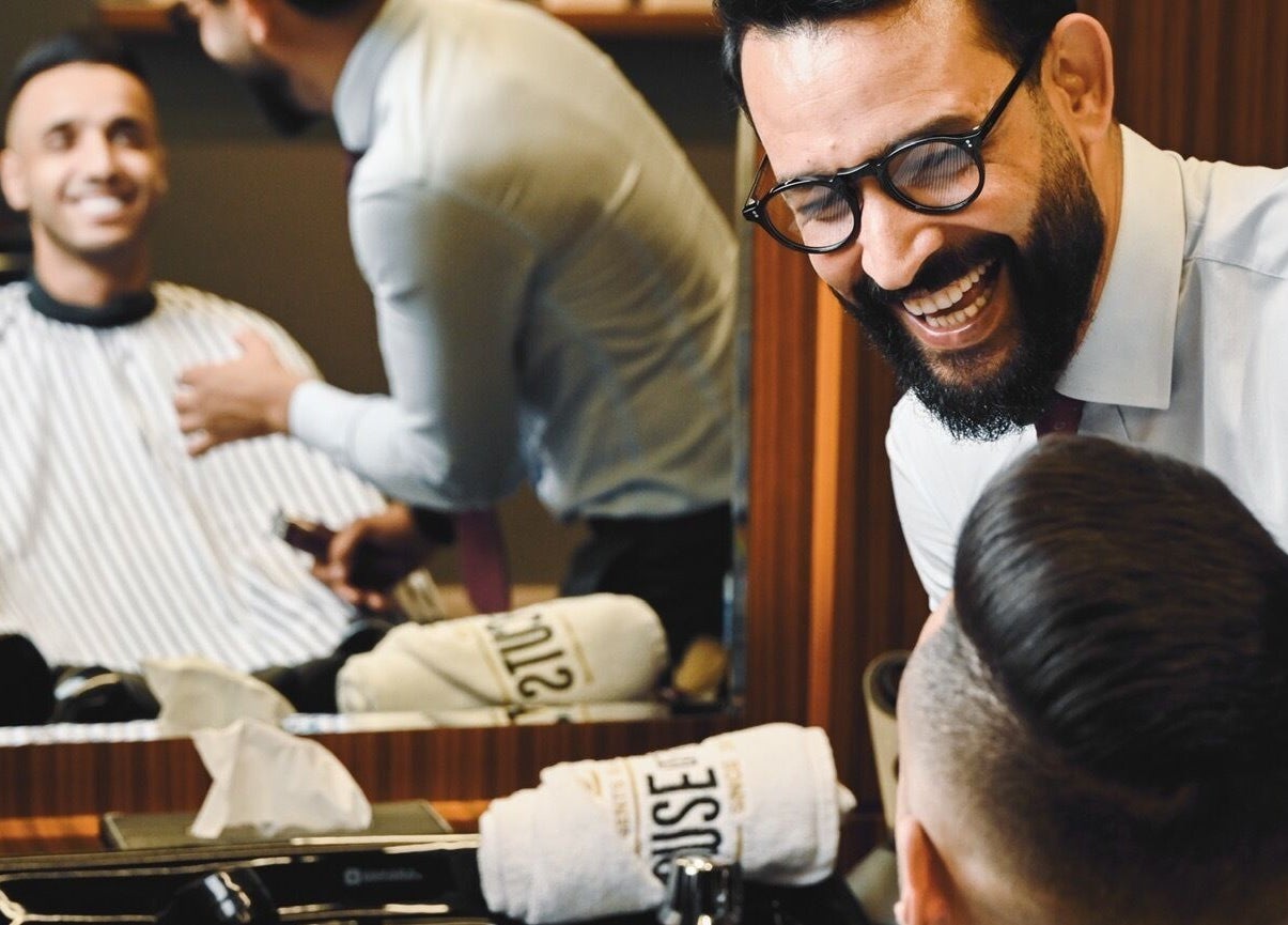 Barber laughing with client in mirror at House of Cuts - Media City, Dubai, Dubai, AE. Modern haircut service.