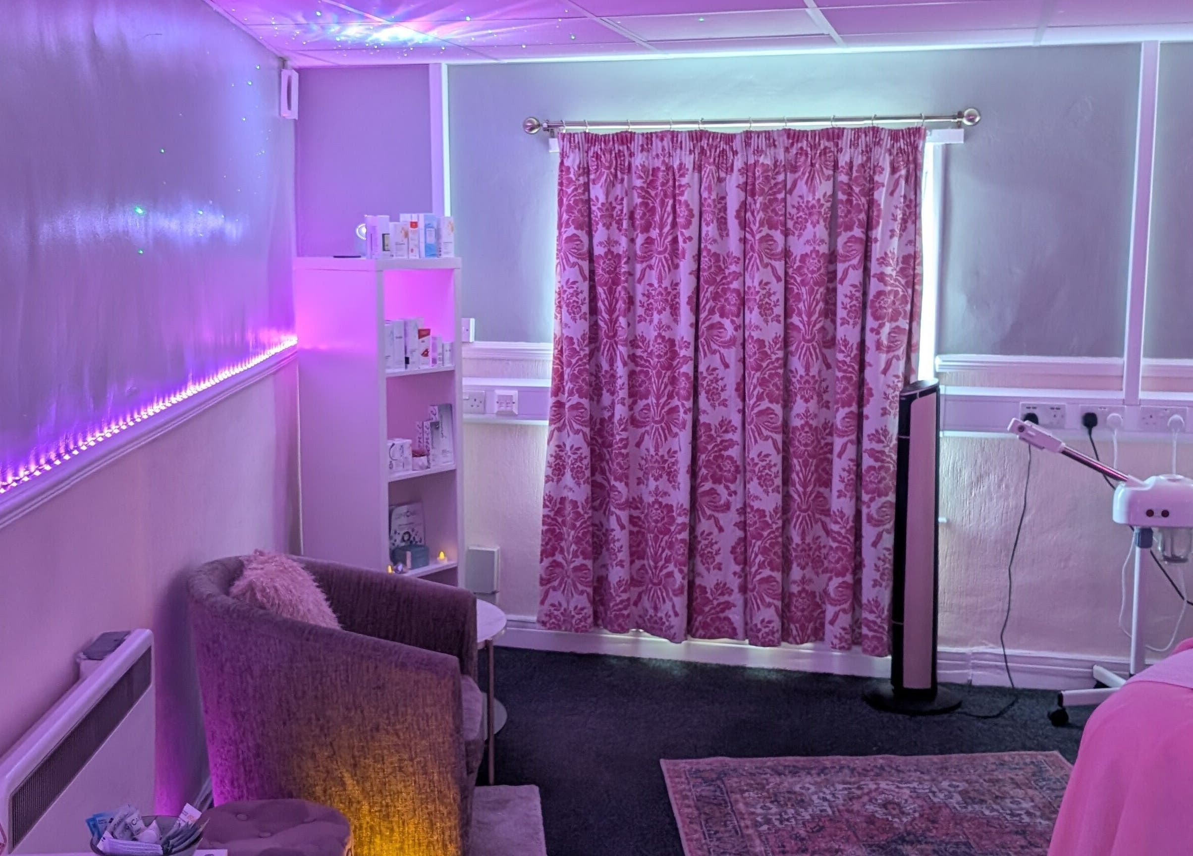 Elegant treatment room at Skinfit Studio, Shifnal, England, GB, featuring soothing pink lighting and floral decor.