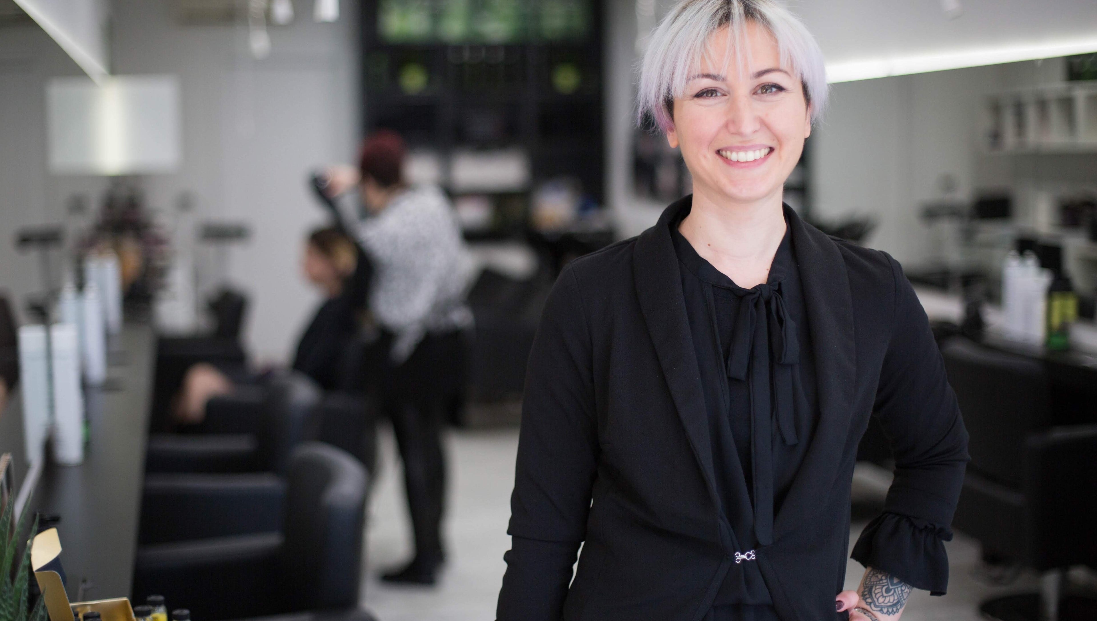 Stilista sorridente presso Elegance Parrucchieri, Pescara, Italia, IT, con clienti sullo sfondo.