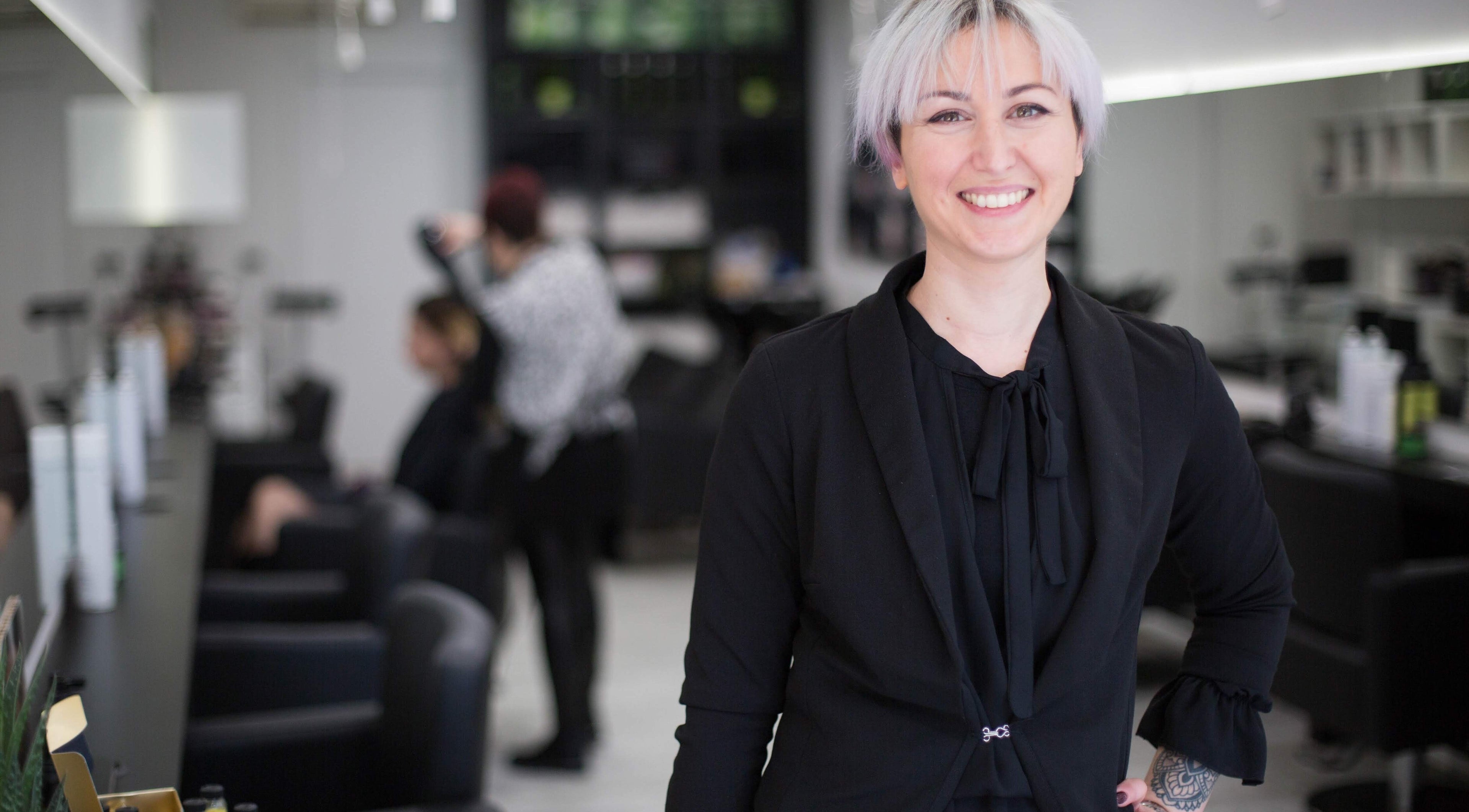 Stilista sorridente presso Elegance Parrucchieri, Pescara, Italia, IT, con clienti sullo sfondo.