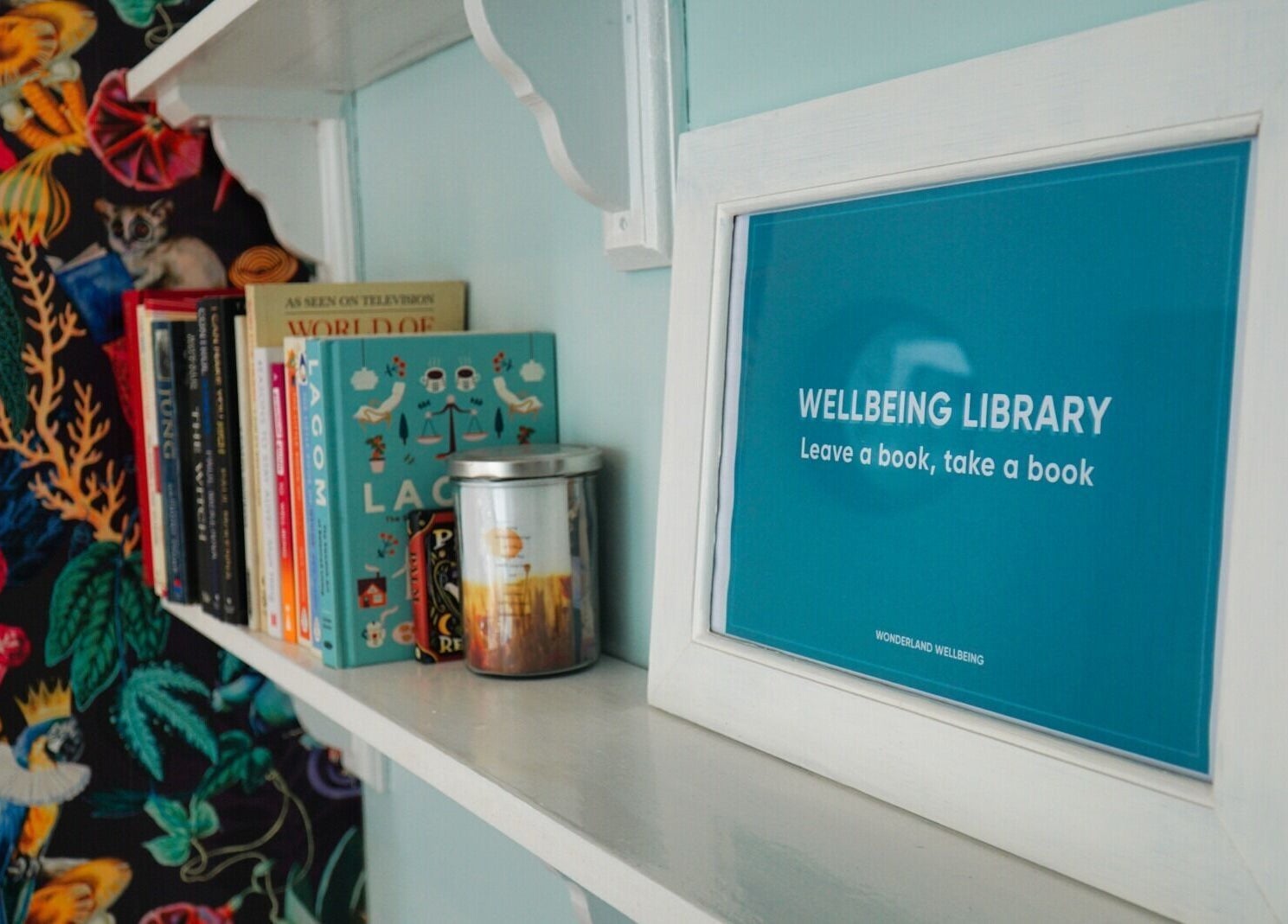 Bookshelf with colorful books and Wellbeing Library sign at Wonderland Wellbeing, North Shields, England, GB.