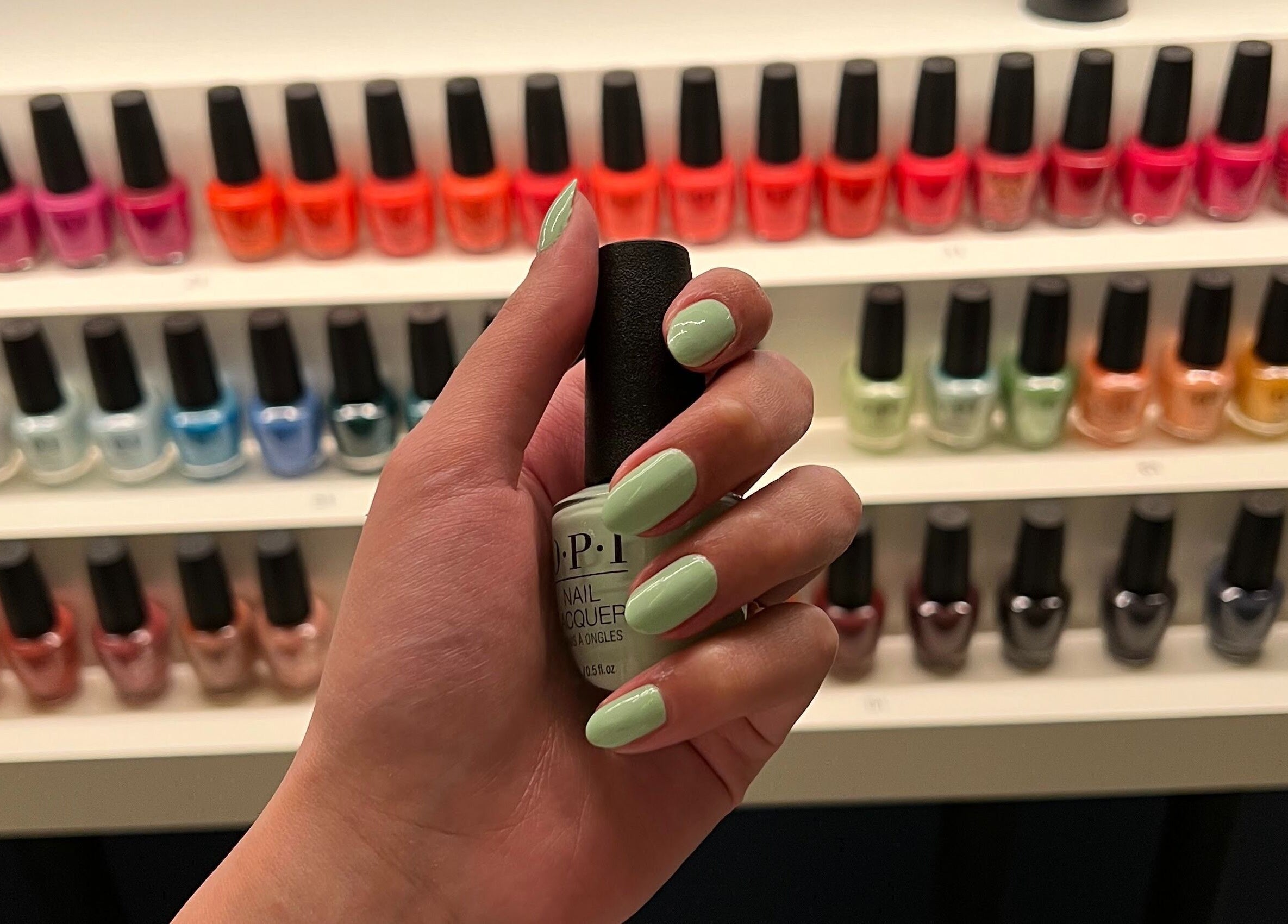 Hand holding nail polish bottle at Circle Nail Bar, Riyadh, Riyadh Province, SA, in front of colorful selection.