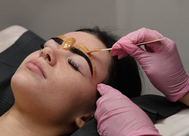 Eyebrow waxing at Beauty at Caitlyn’s, Harrington Park, New South Wales, AU with pink gloves applying wax.