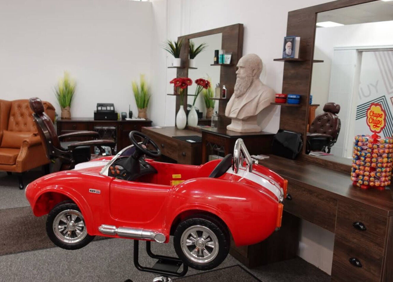 Child's red car seat beside vintage-style chairs at Darwin's Barbers, Shrewsbury, England, GB.