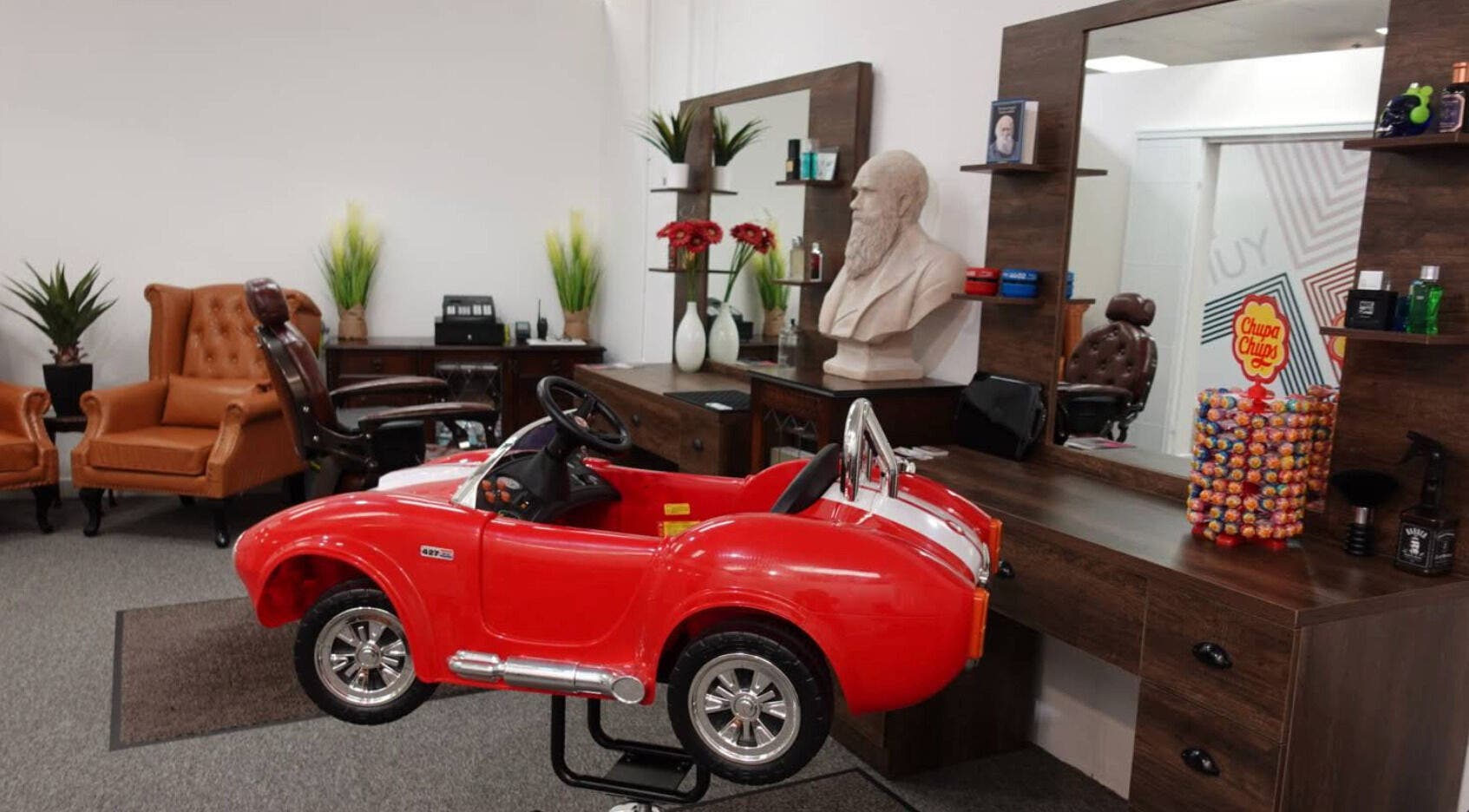 Child's red car seat beside vintage-style chairs at Darwin's Barbers, Shrewsbury, England, GB.