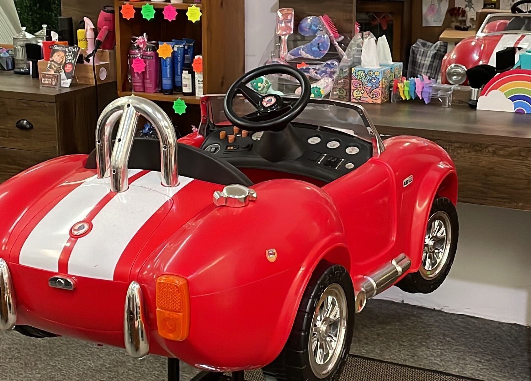 Child's barber car chair at Darwin's Barbers, Shrewsbury, England, GB. Red car seat enhances salon visit for kids.