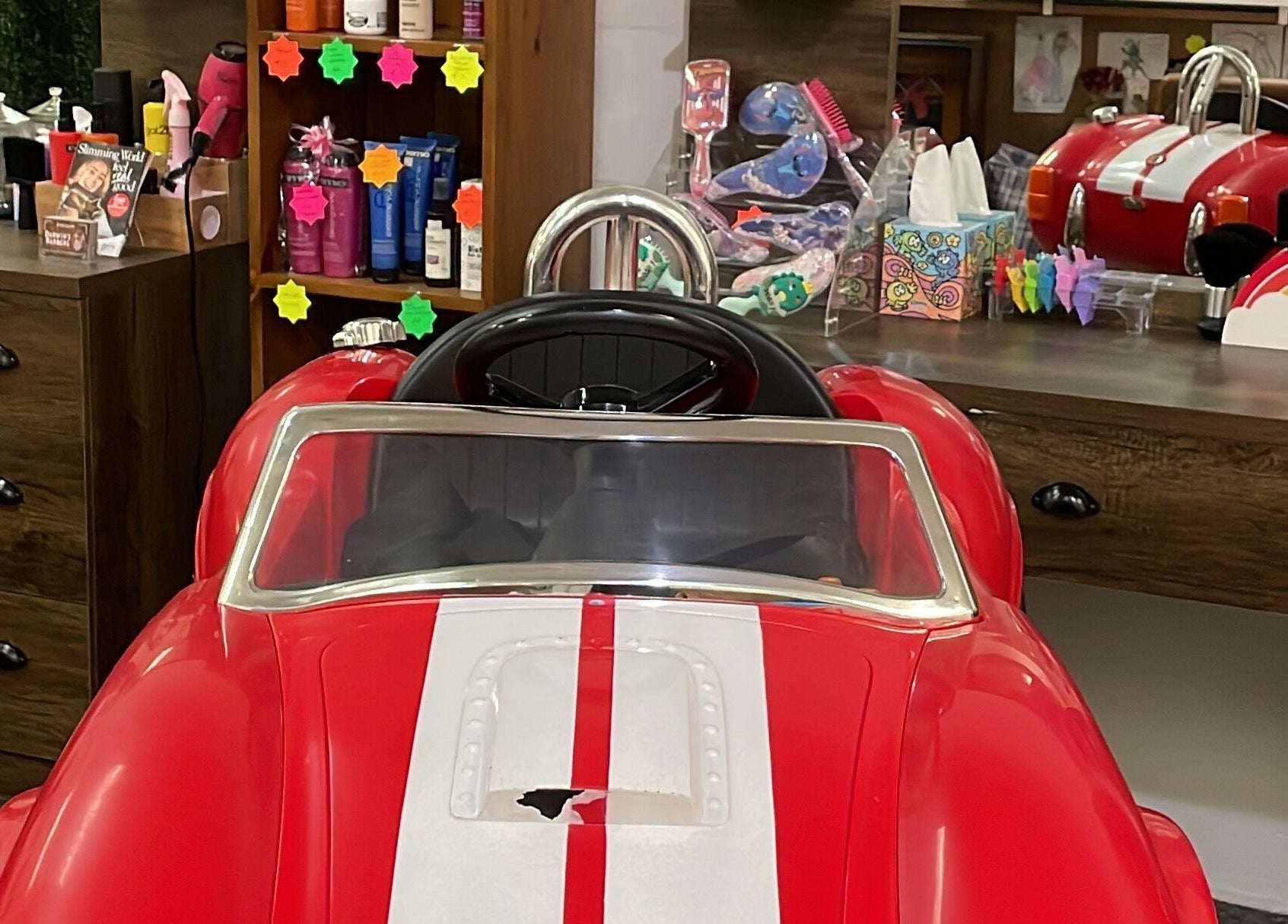 Children's barber chair in a car shape at Darwin's Barbers, Shrewsbury, England, GB, surrounded by products.