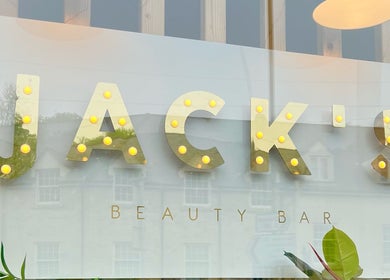 Brightly lit sign of JACK’S Beauty Bar, Nailsworth, England reflecting a charming street view.