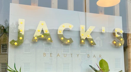 Brightly lit sign of JACK’S Beauty Bar, Nailsworth, England reflecting a charming street view.