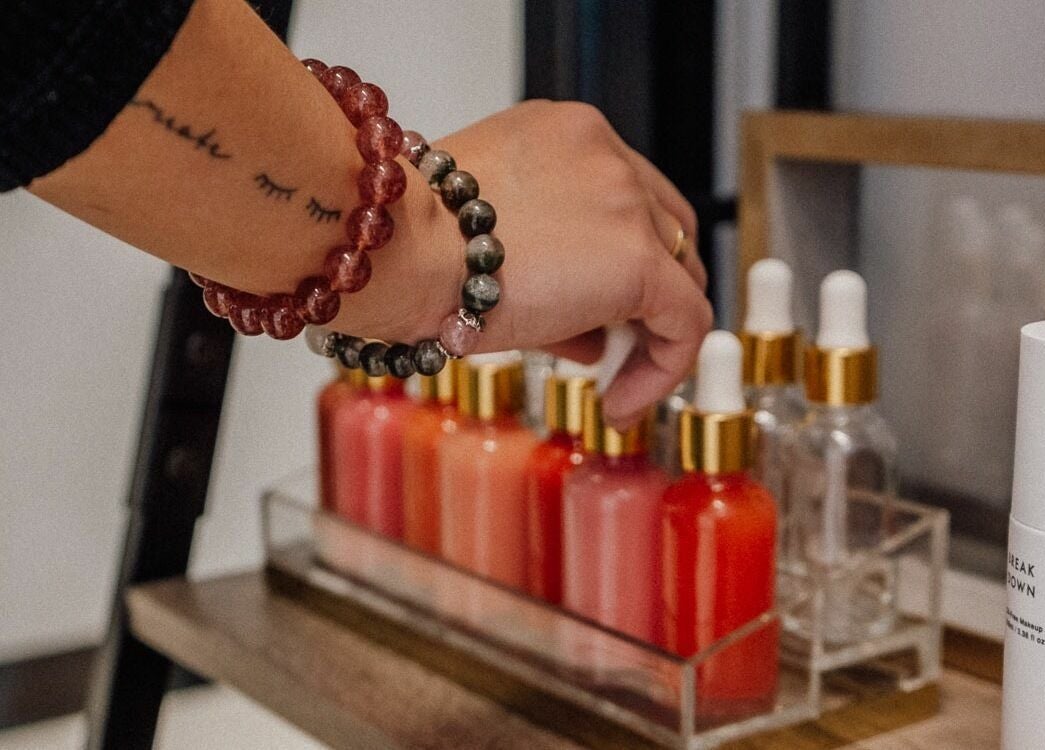 A hand reaches for colorful serum bottles at Glam by Dang, New York, New York, US highlighting beauty products.