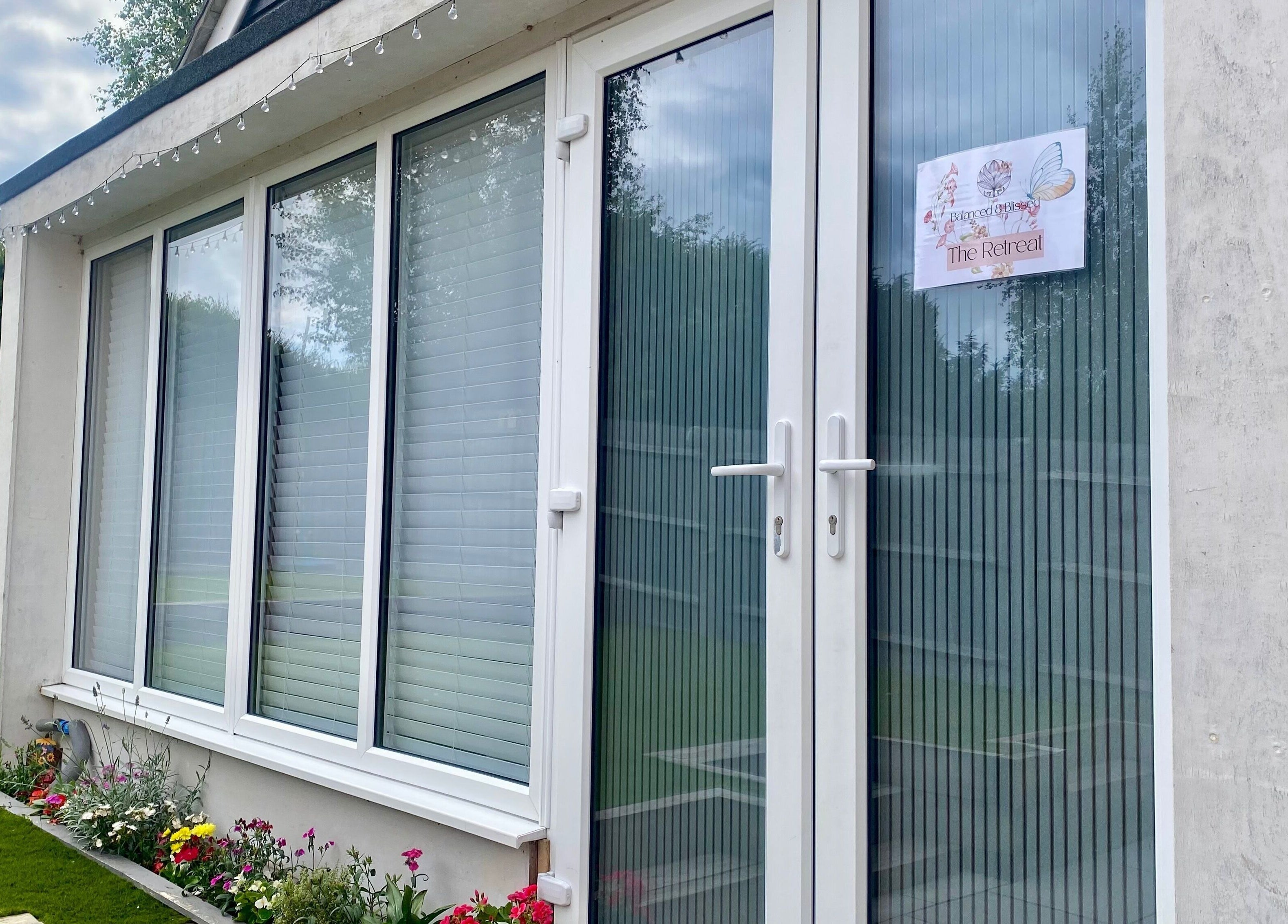 White-framed glass doors at Balanced & Blissed - The Retreat in Whitfield, England, GB surrounded by greenery.