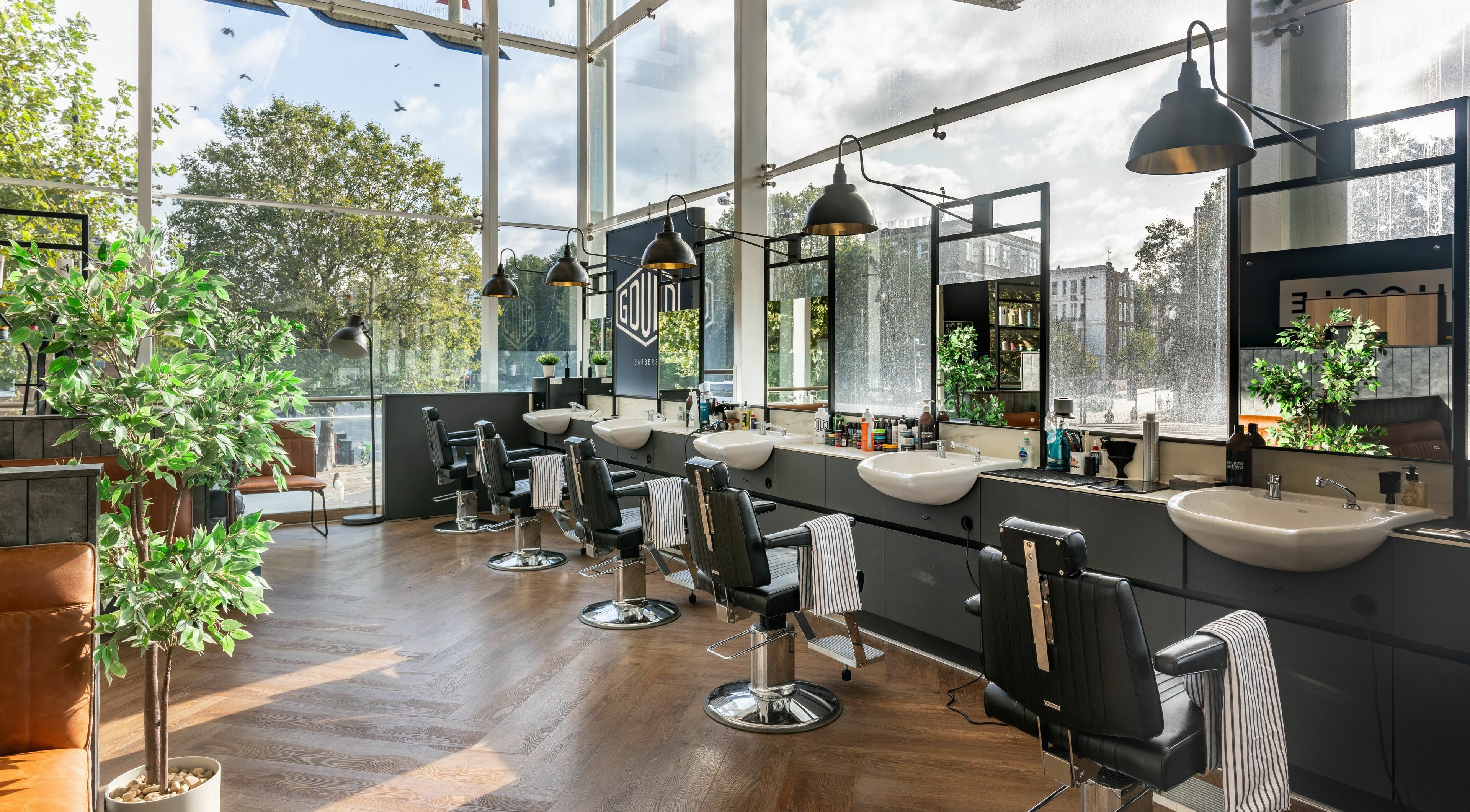 Interior of Gould Barbers London (Kensington) in London, England, GB featuring sleek barber stations and lush greenery.