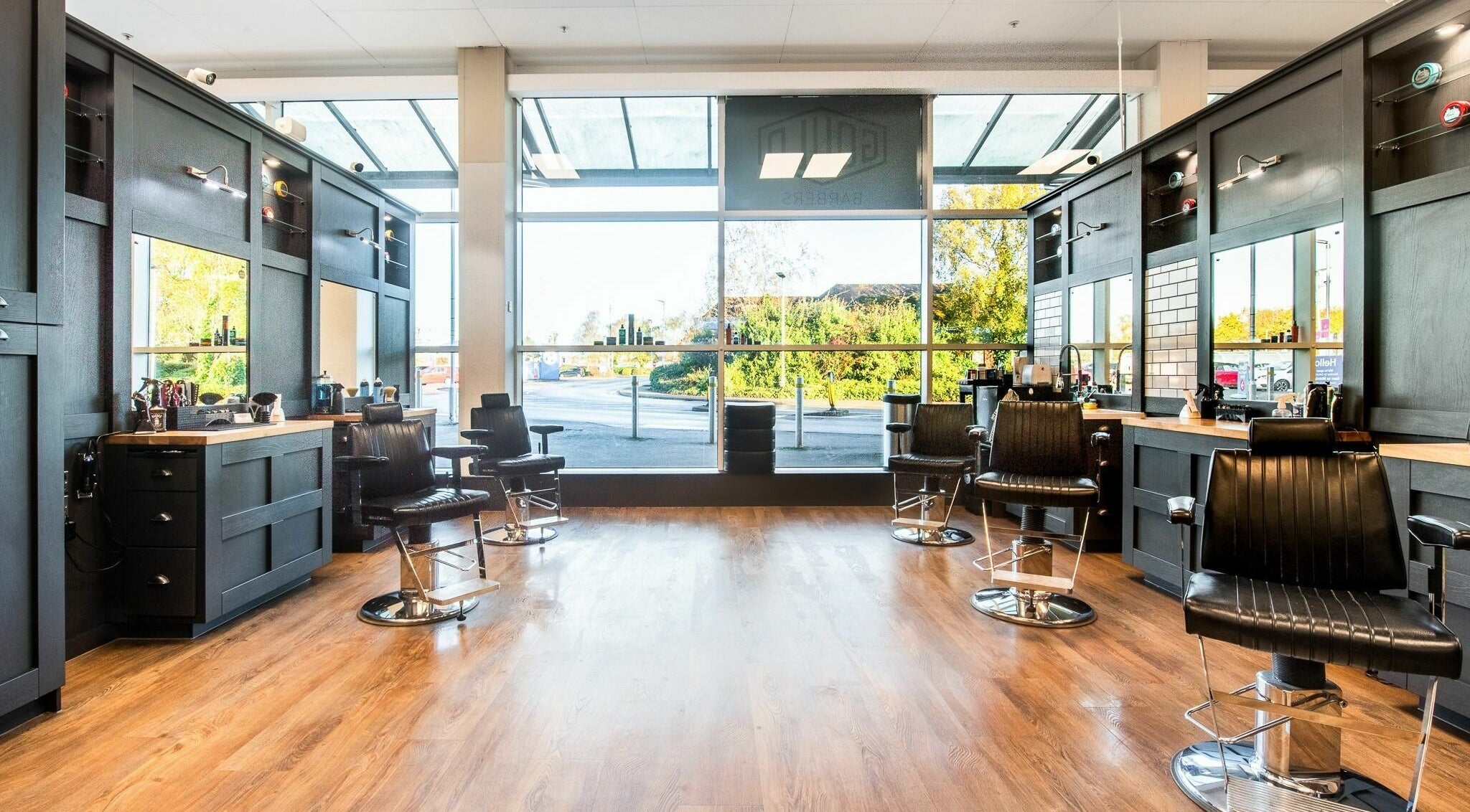 Bright, modern interior of Gould Barbers Newbury, Newbury, England, GB with sleek black chairs and large windows.