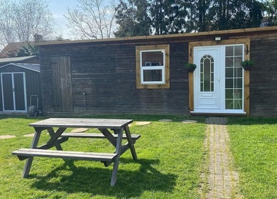 Peaceful garden at LavenderBlue HQ, Herne Bay, England with wooden building and picnic table.