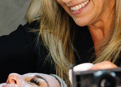 Beauty treatment at Permalicious Ink, Beauty and Aesthetics in Sandton, Gauteng, ZA. Smiling aesthetician applies face mask.